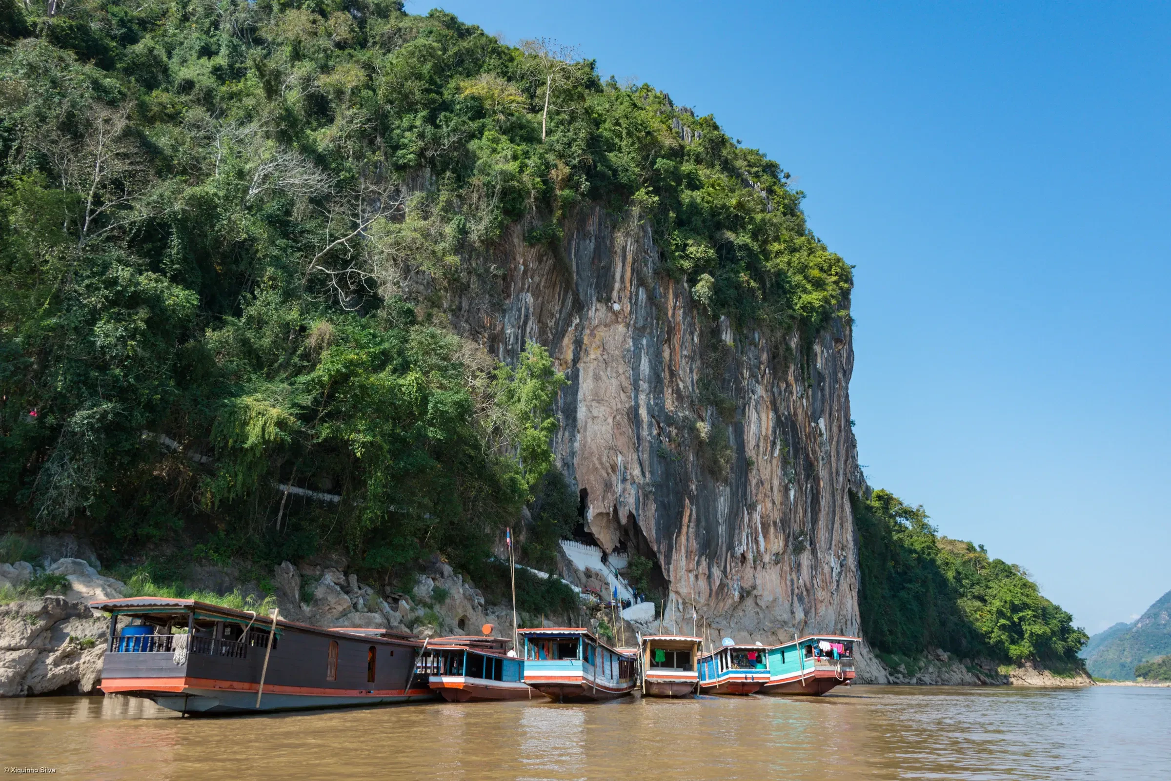 Slow boats moored below the limestone cliff of the Pak Ou Caves on the Mekong