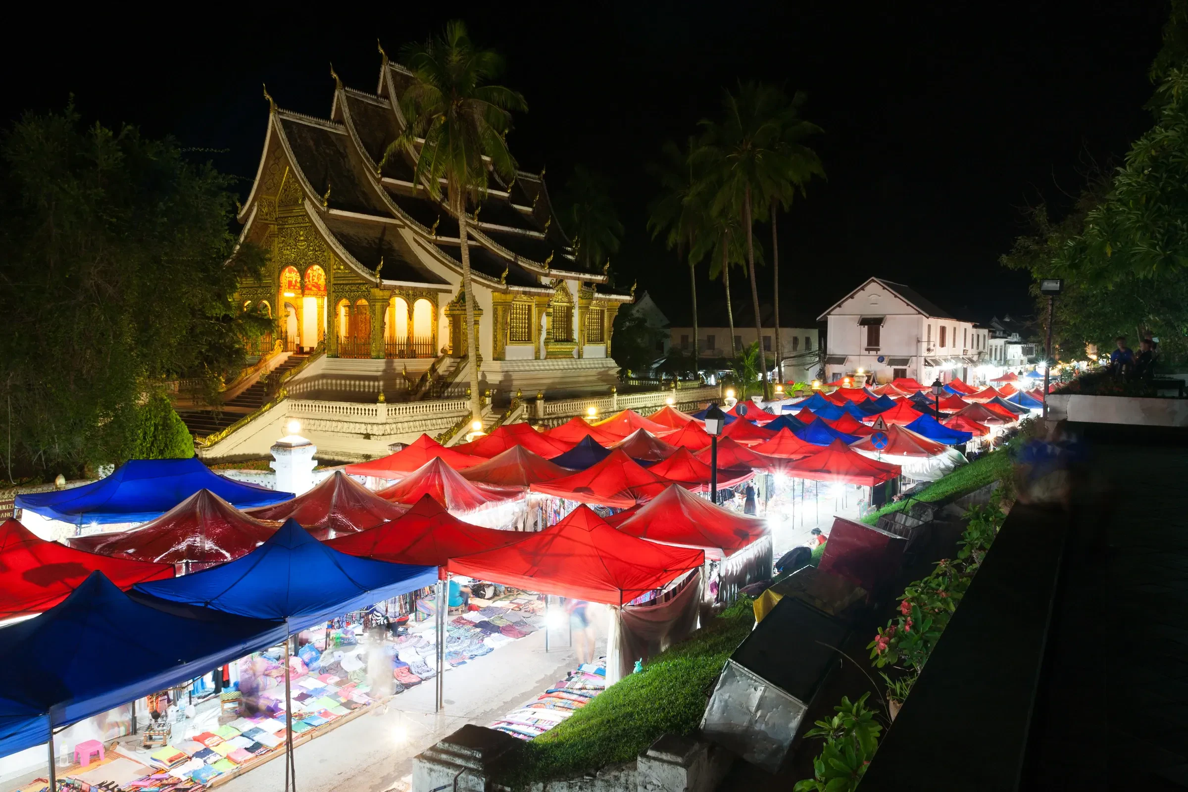 Luang Prabang's night market stalls under red and blue awnings, with a lit temple roof behind