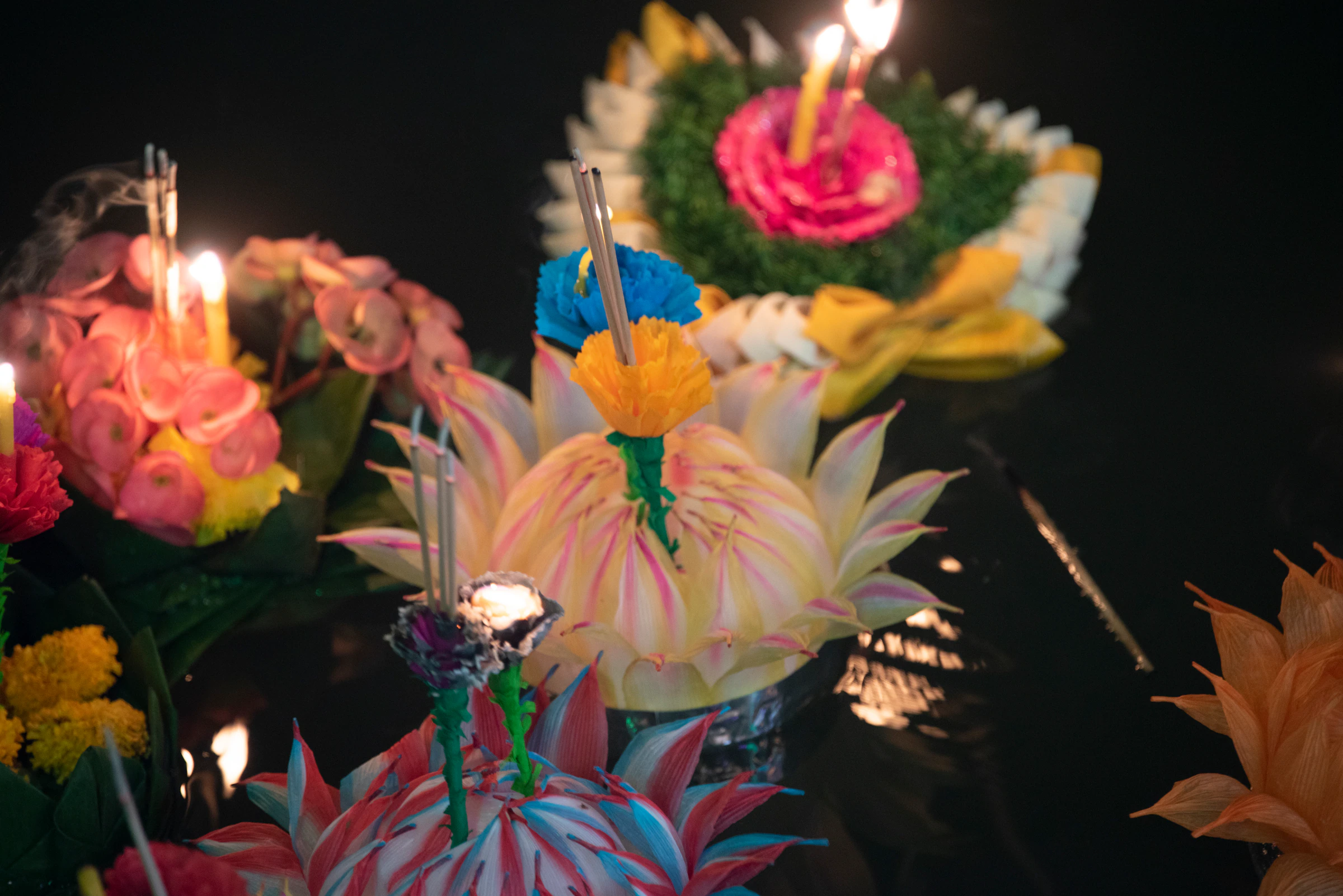 Krathongs of folded banana leaf and flowers with lit candles, seen close up at night
