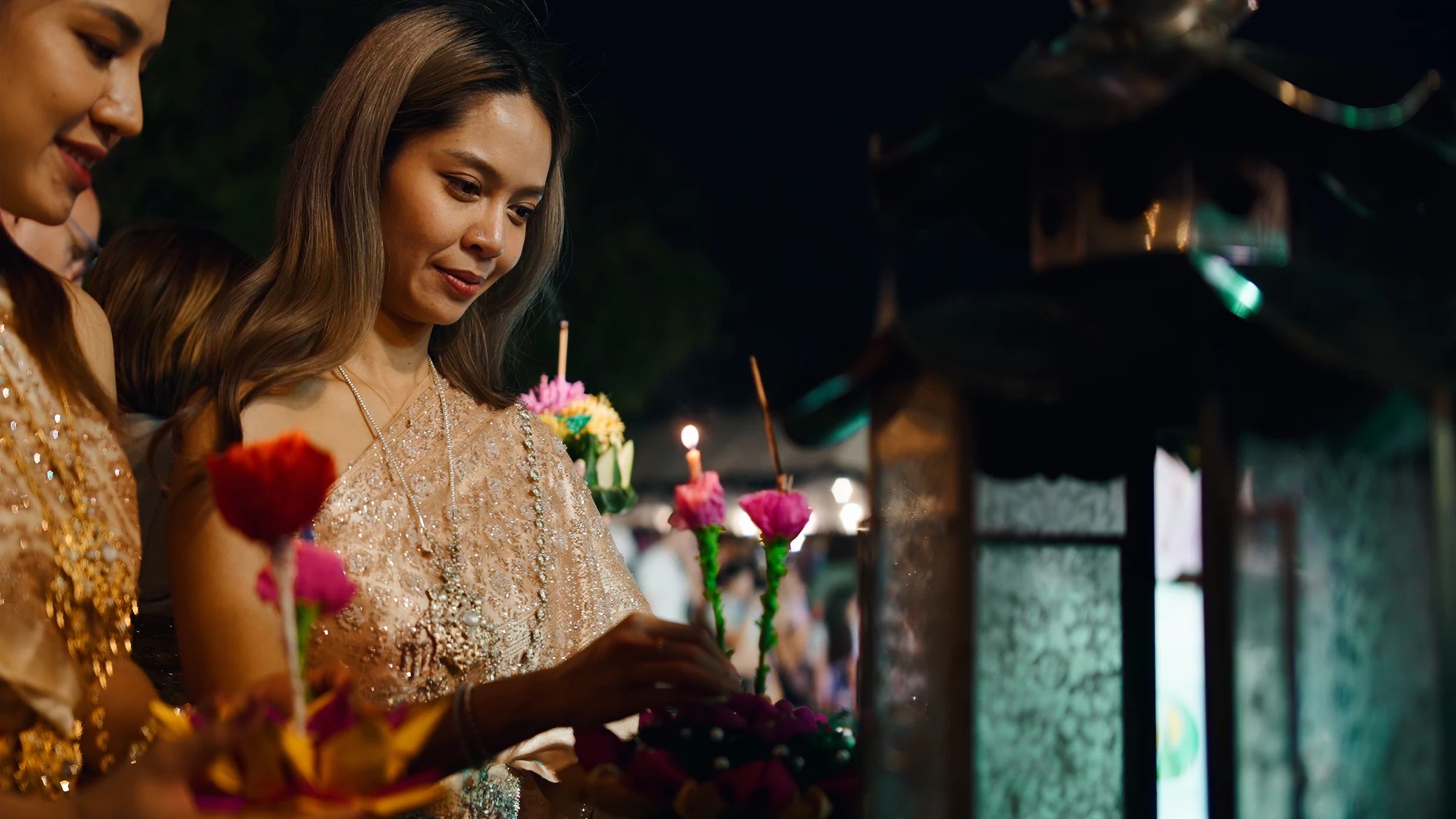A woman in a gold traditional dress holding a flower krathong at night