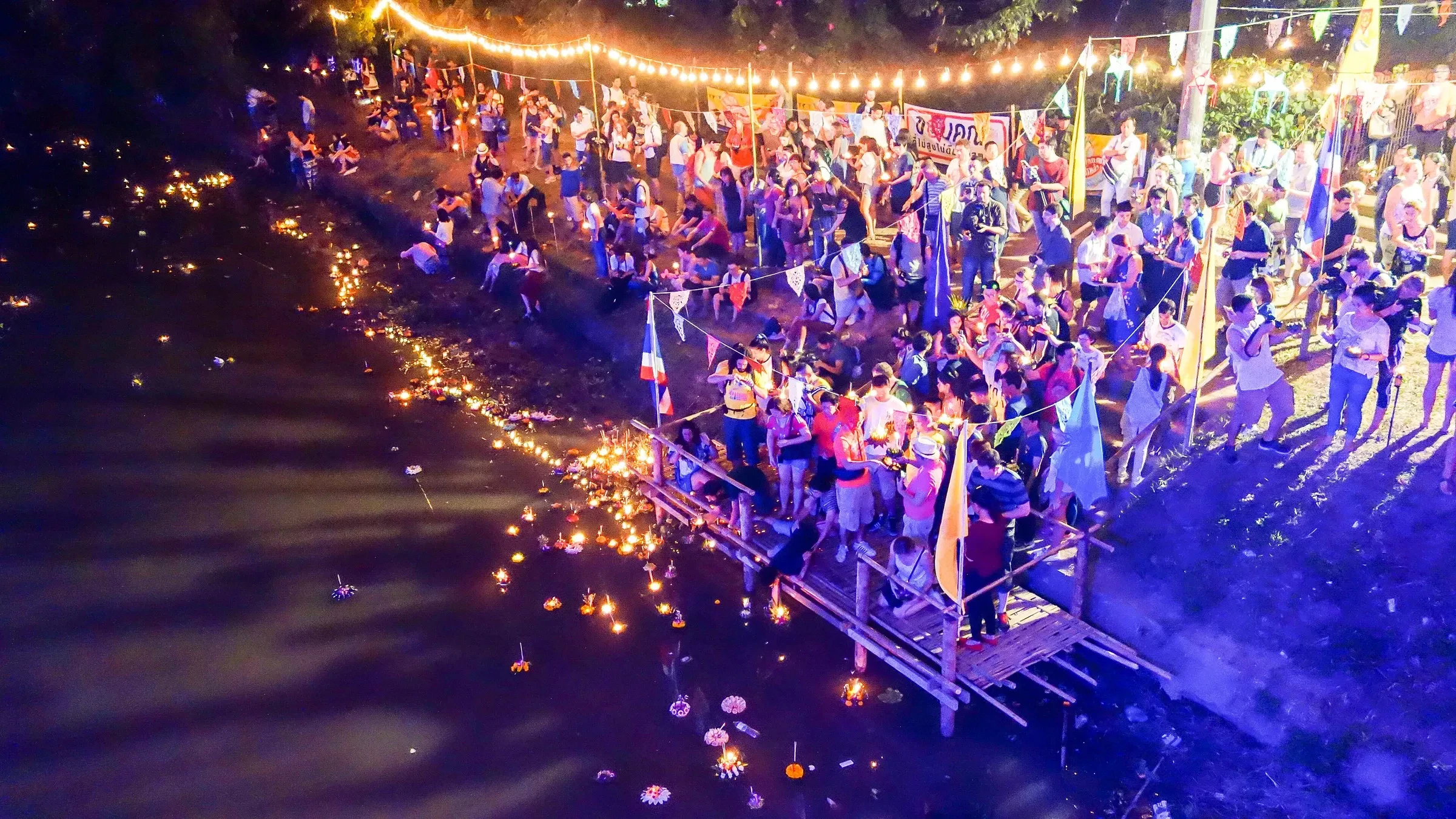 A crowd gathered at the river's edge in Chiang Mai as krathongs and lights float on the water