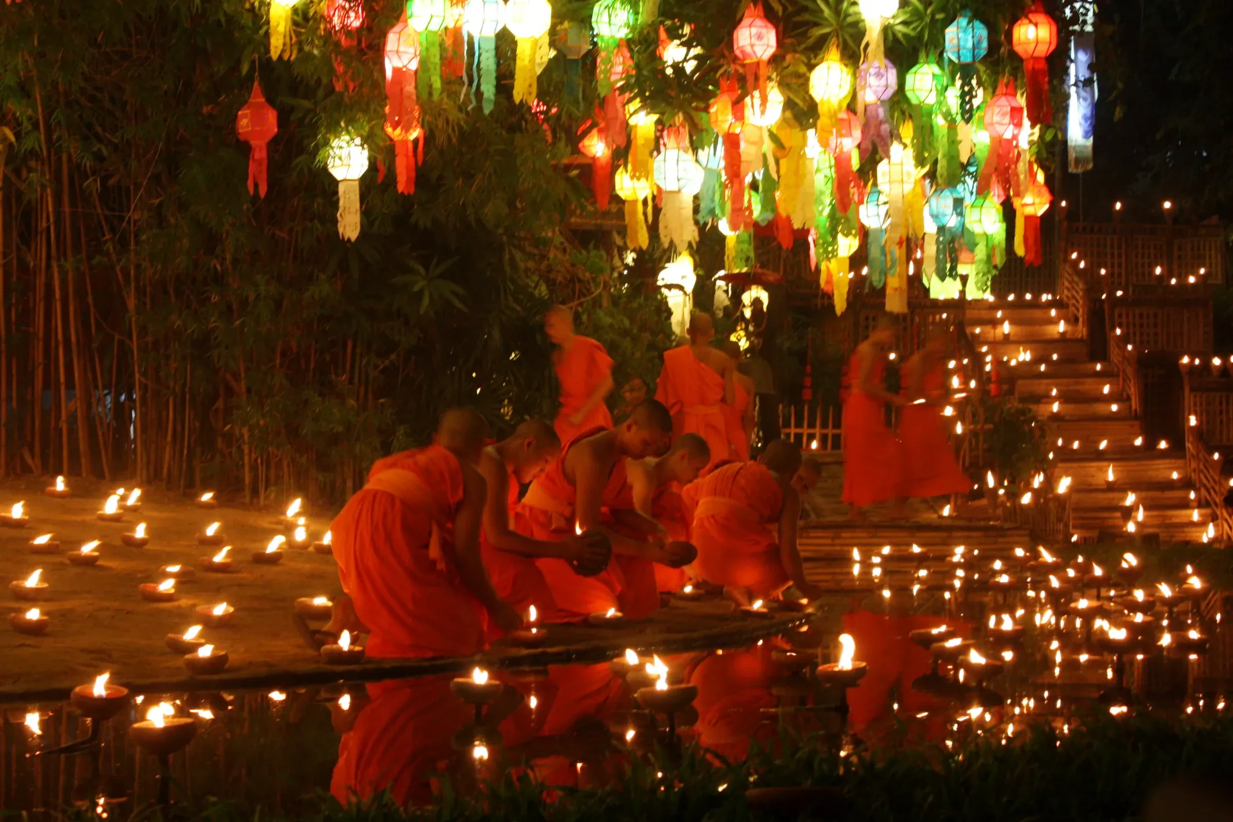 Buddhist monks sitting among rows of candles under hanging lanterns at a temple in Chiang Mai