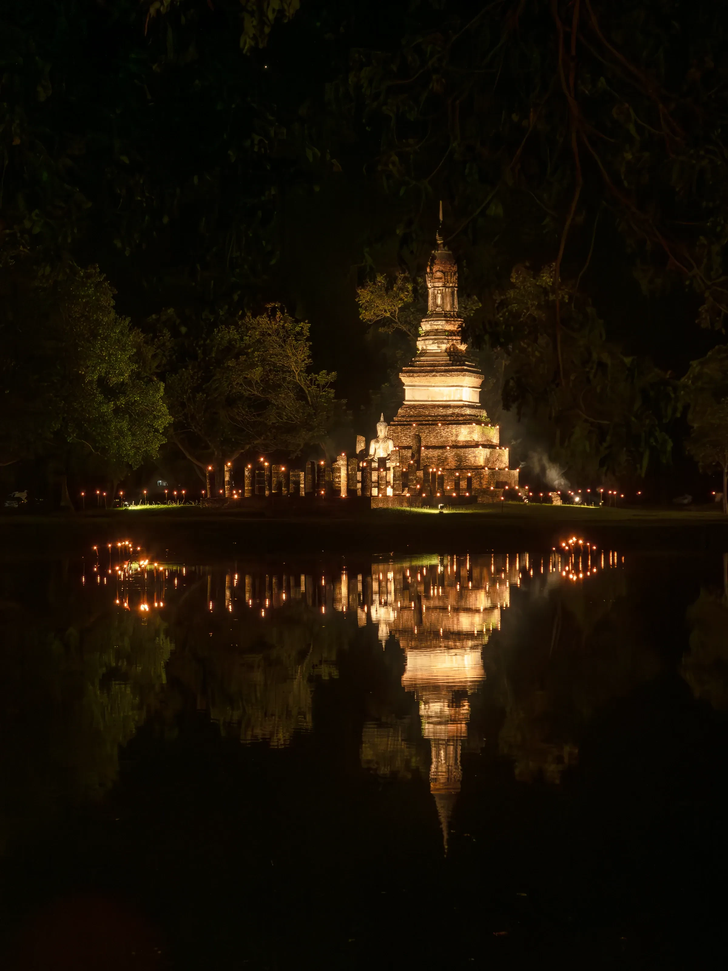 Wat Traphang Ngoen in Sukhothai reflected in a pond, lit up for Loy Krathong