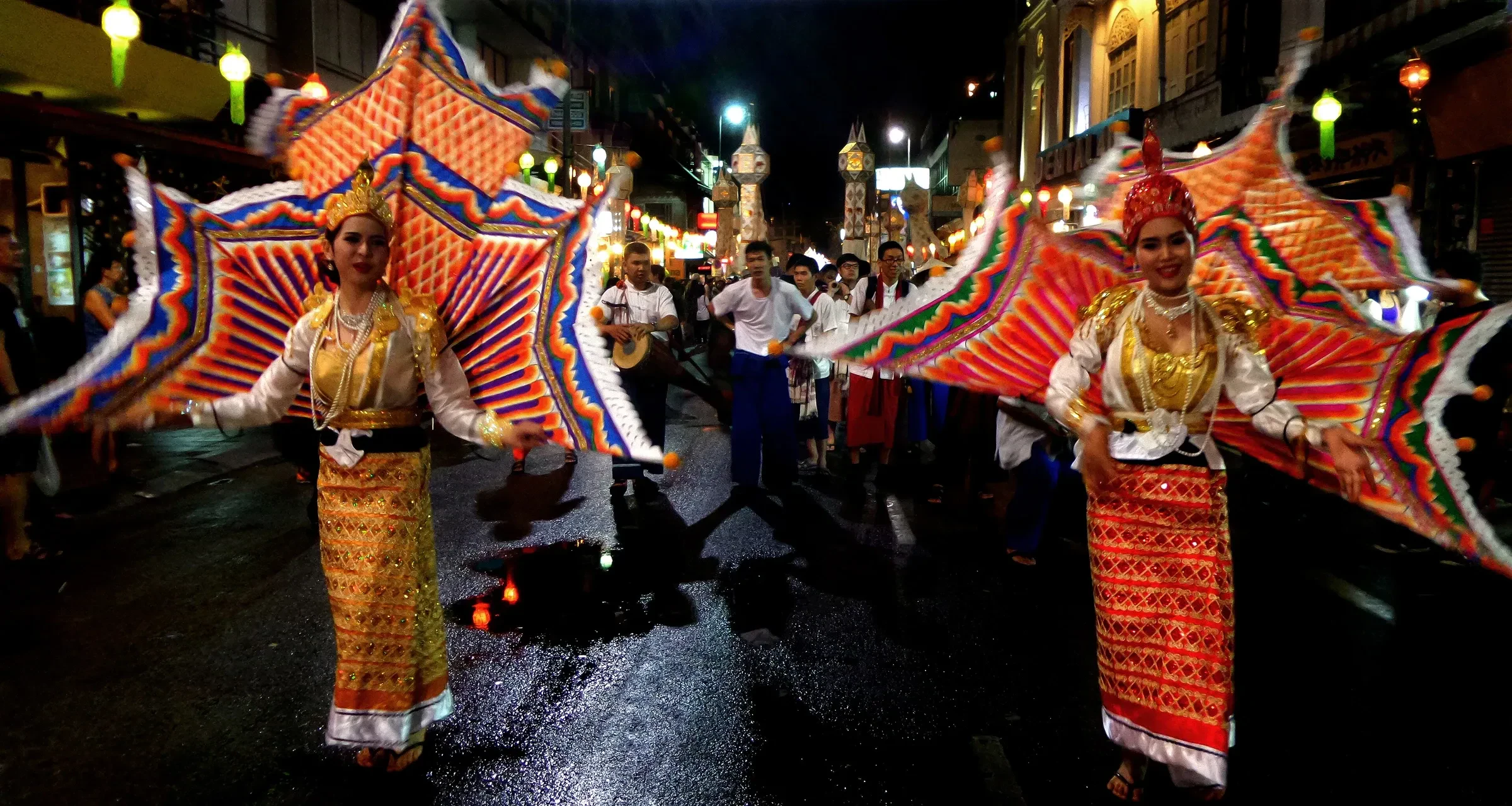 Dancers in costume with large fan-shaped wings walking in a night parade in Chiang Mai during Loy Krathong