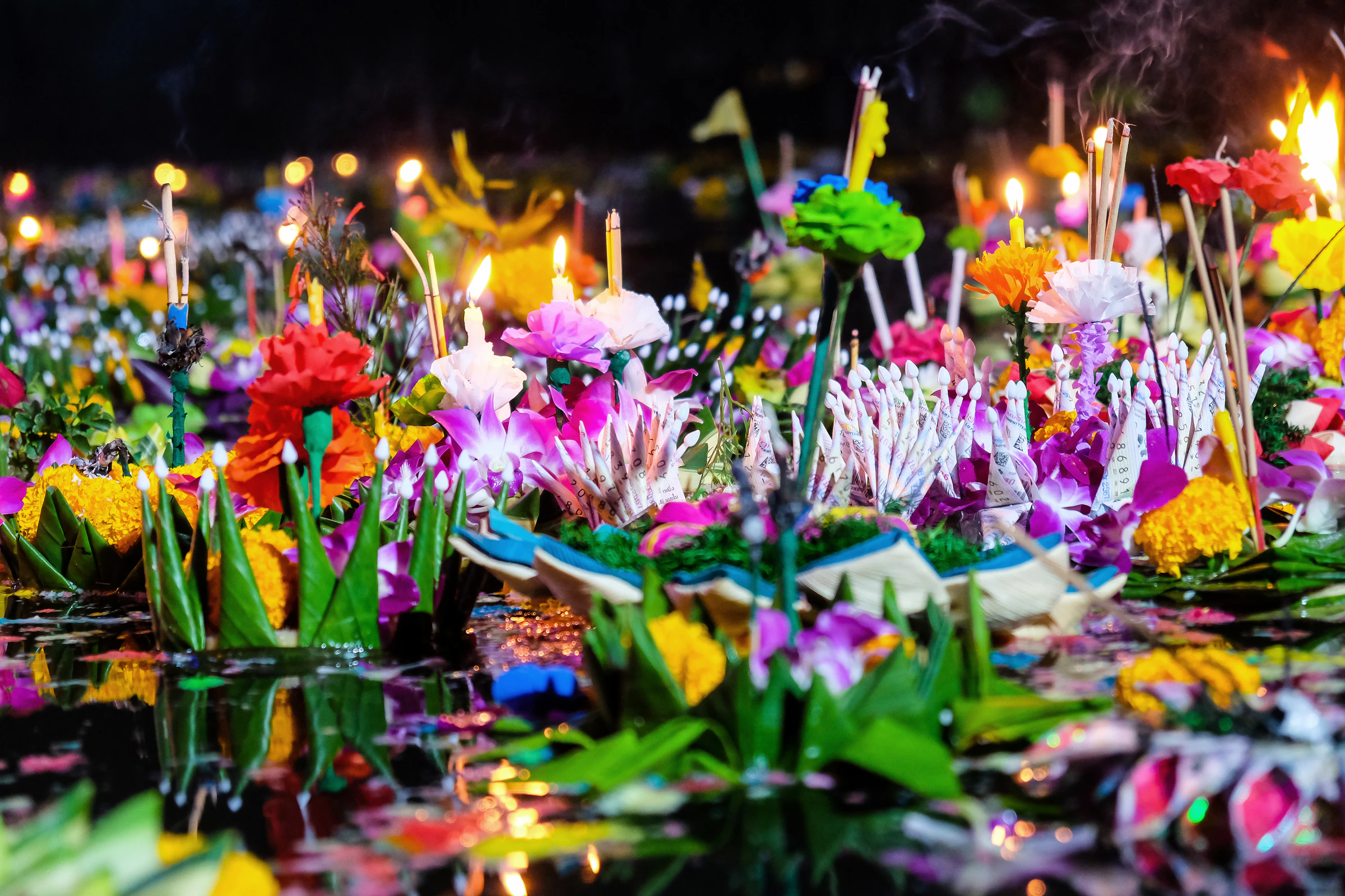 Candle-lit krathongs made of banana leaves and flowers floating on a river at night
