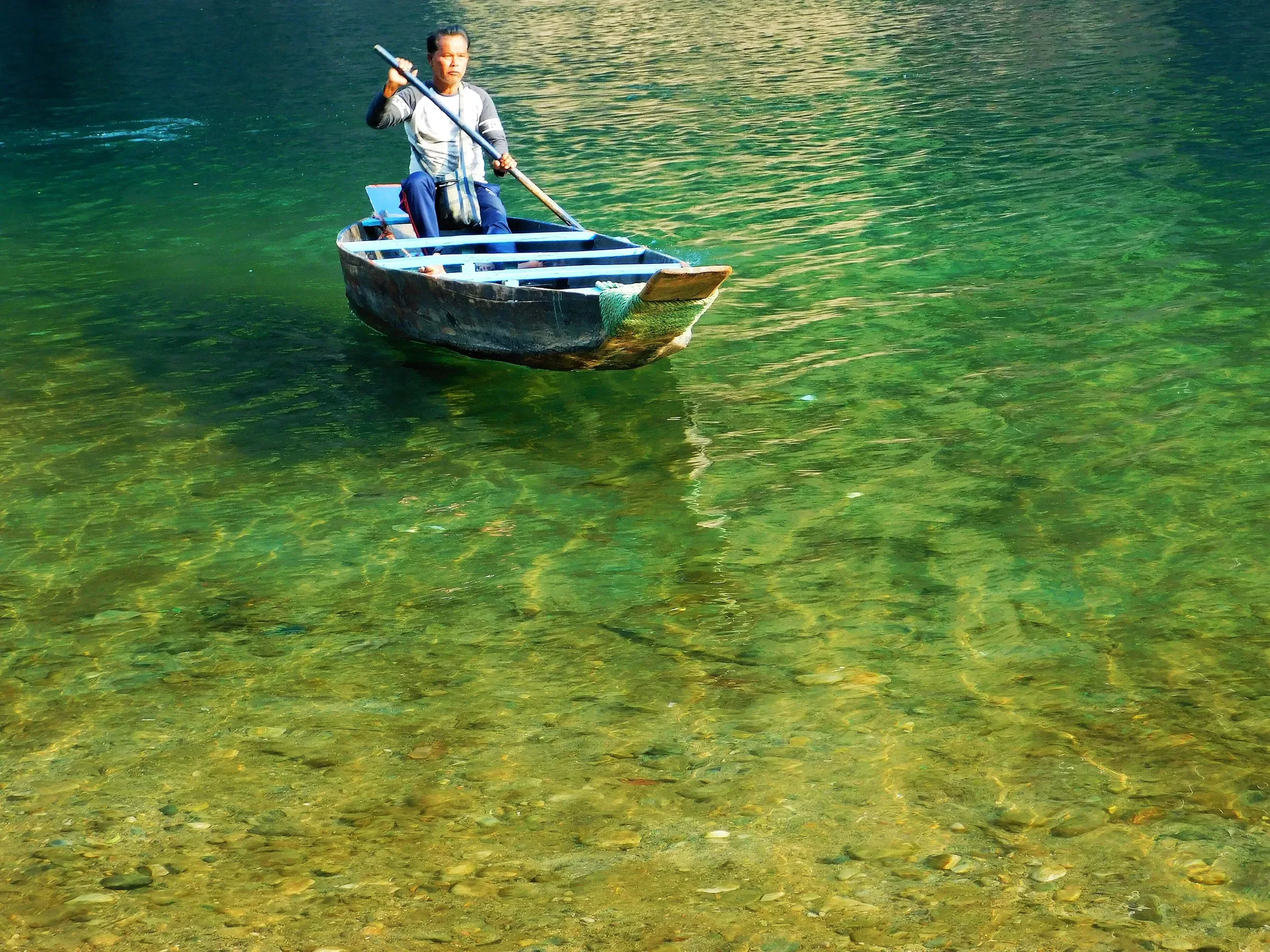 A wooden boat on the clear green water of the Umngot River at Dawki