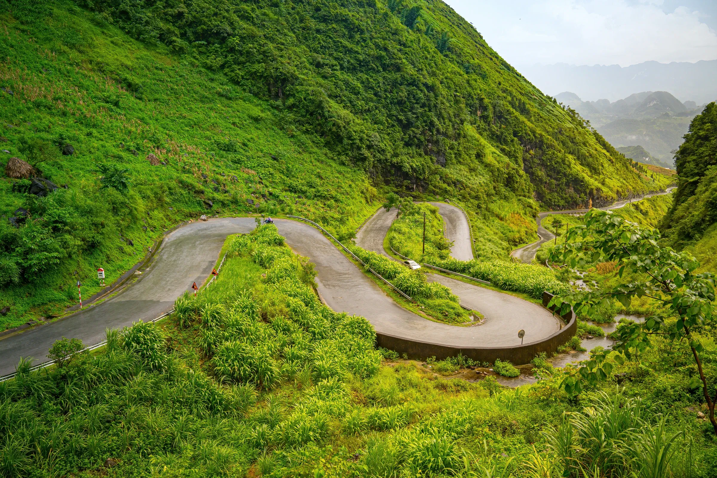 A curving mountain road winding across a green hillside near Tham Ma Pass on the Ha Giang Loop