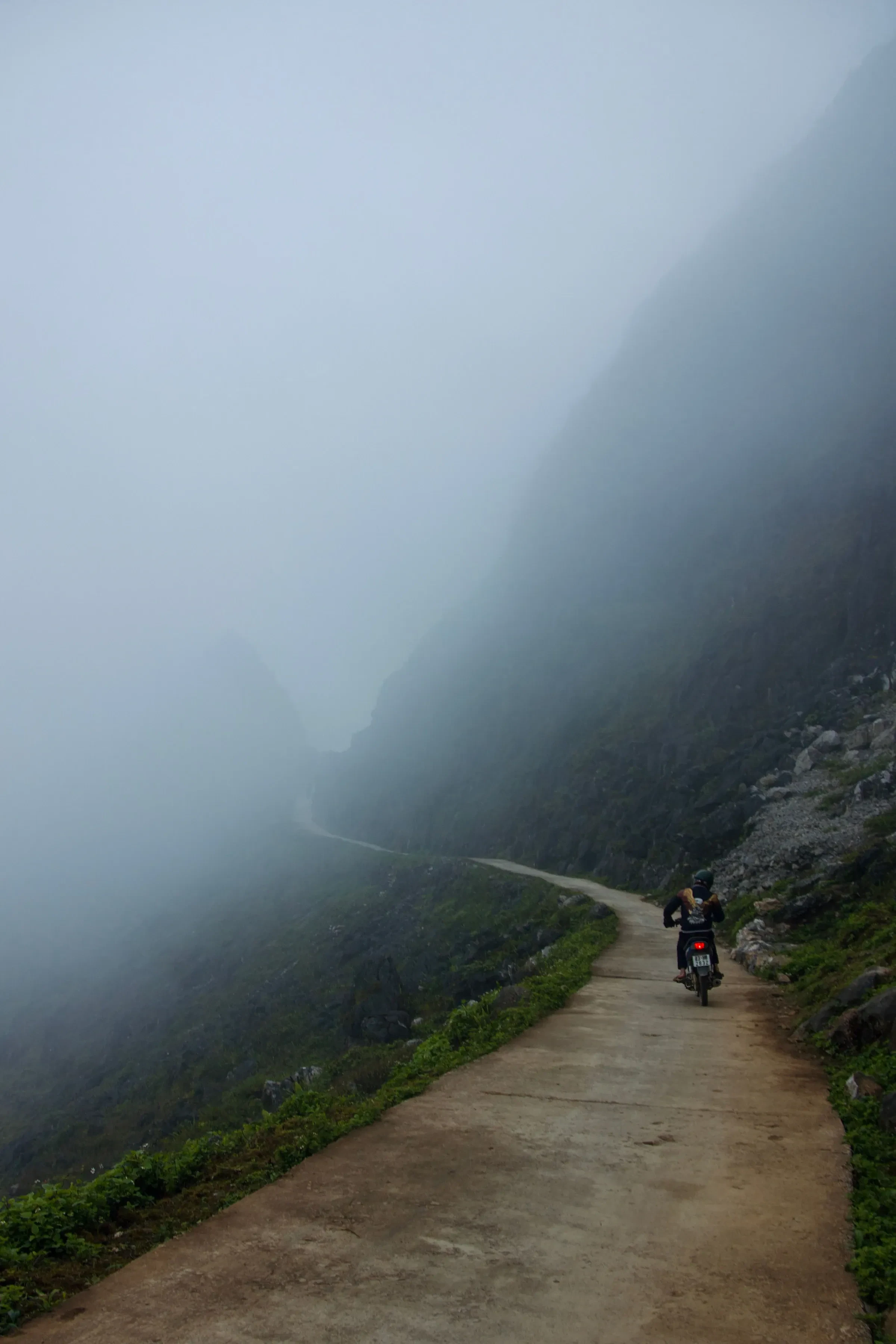 A rider in a helmet on a narrow mountain road in thick fog in northern Vietnam