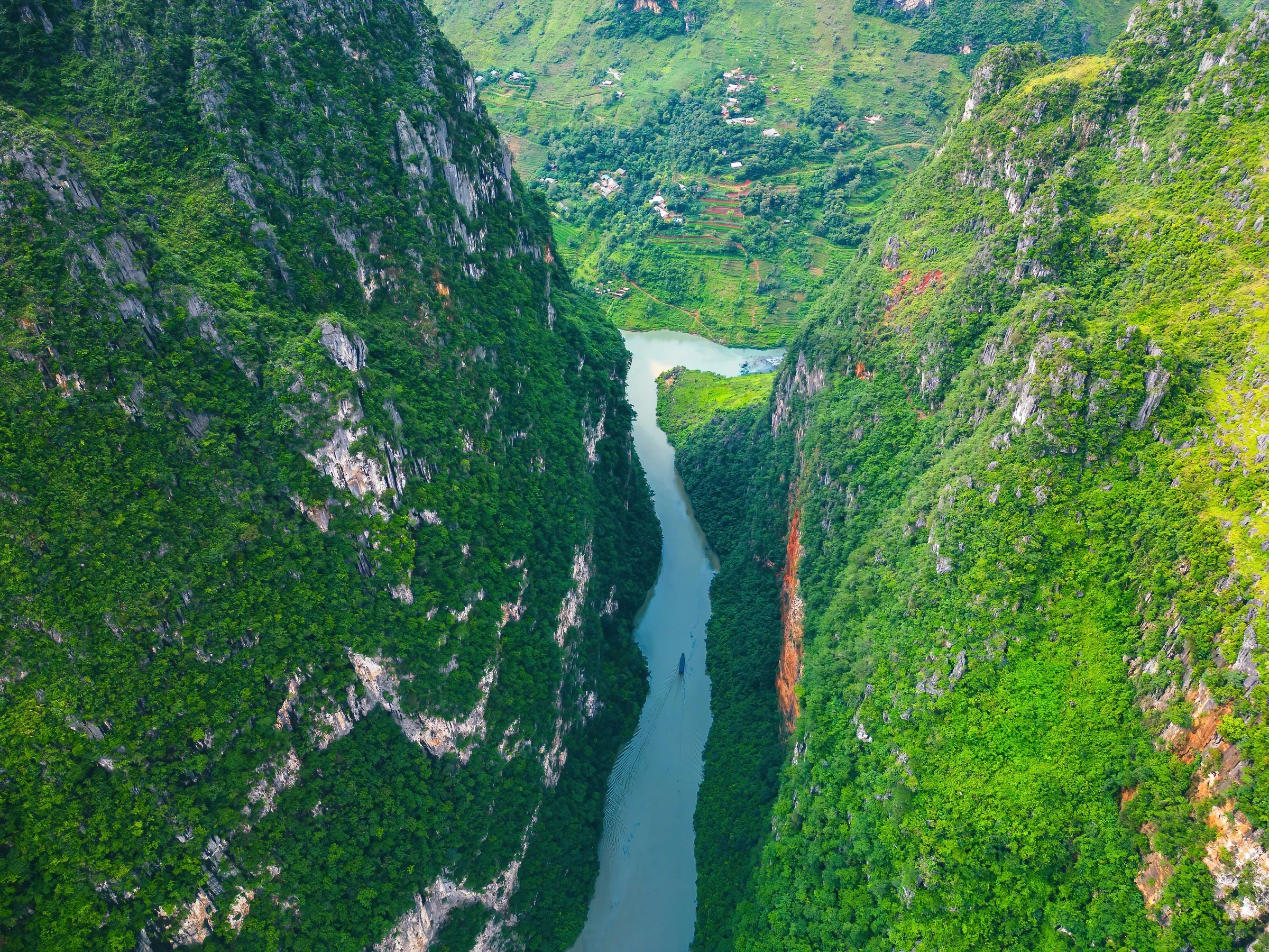 Aerial view of the Nho Que River on a foggy morning, with tourist boats on the emerald water