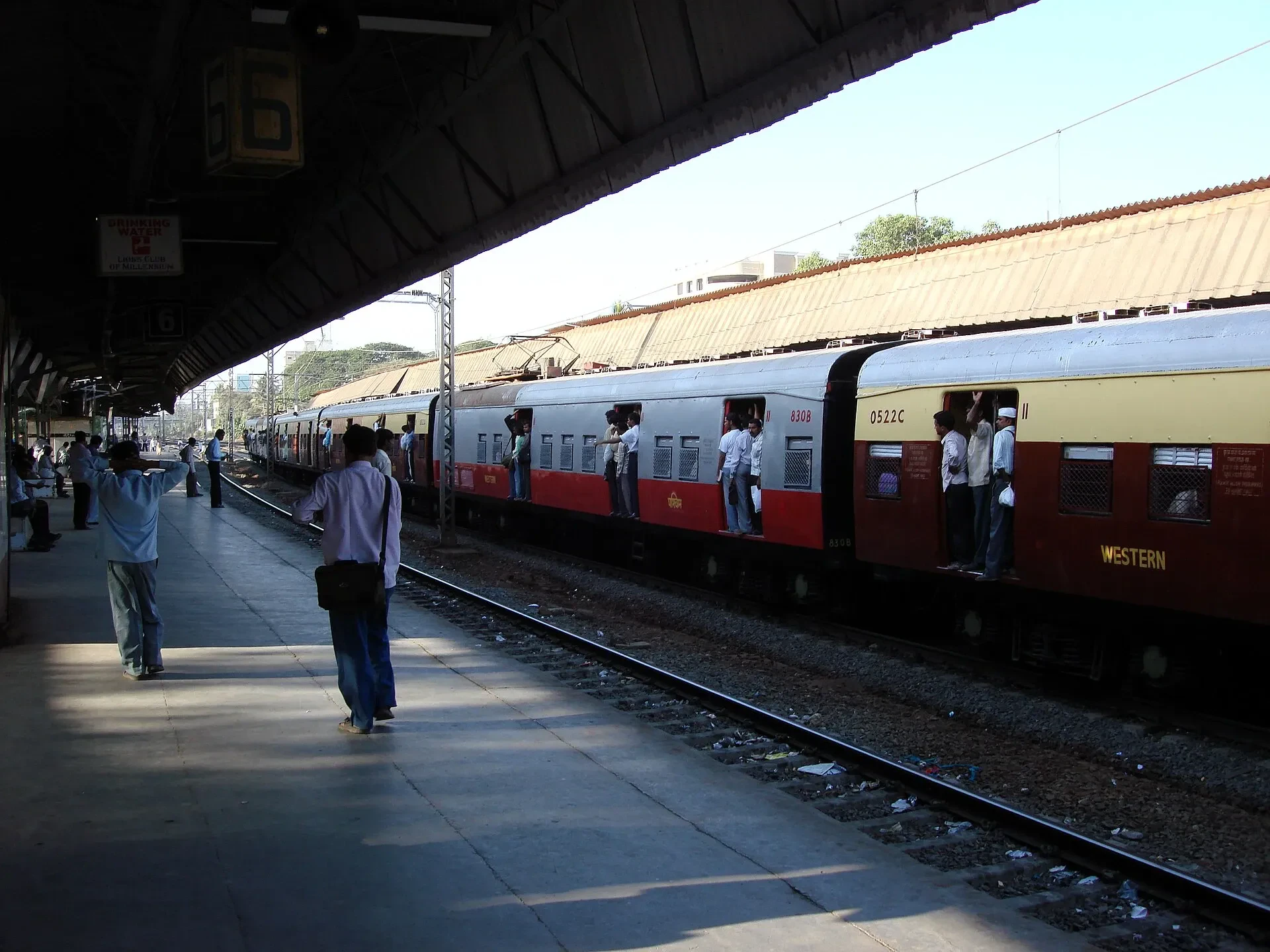 A suburban train standing at a Mumbai station platform, with passengers on the platform and in the open doorways