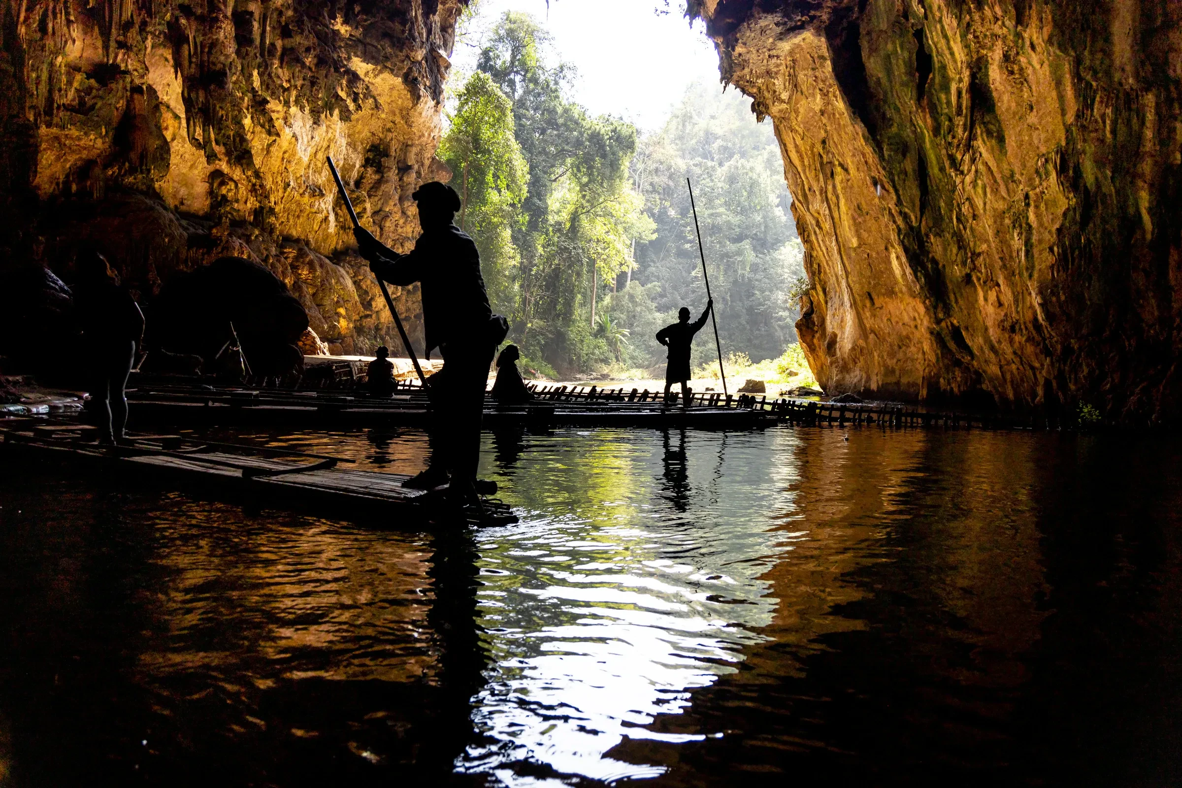 Silhouetted people on bamboo rafts on the underground river inside Tham Lod cave