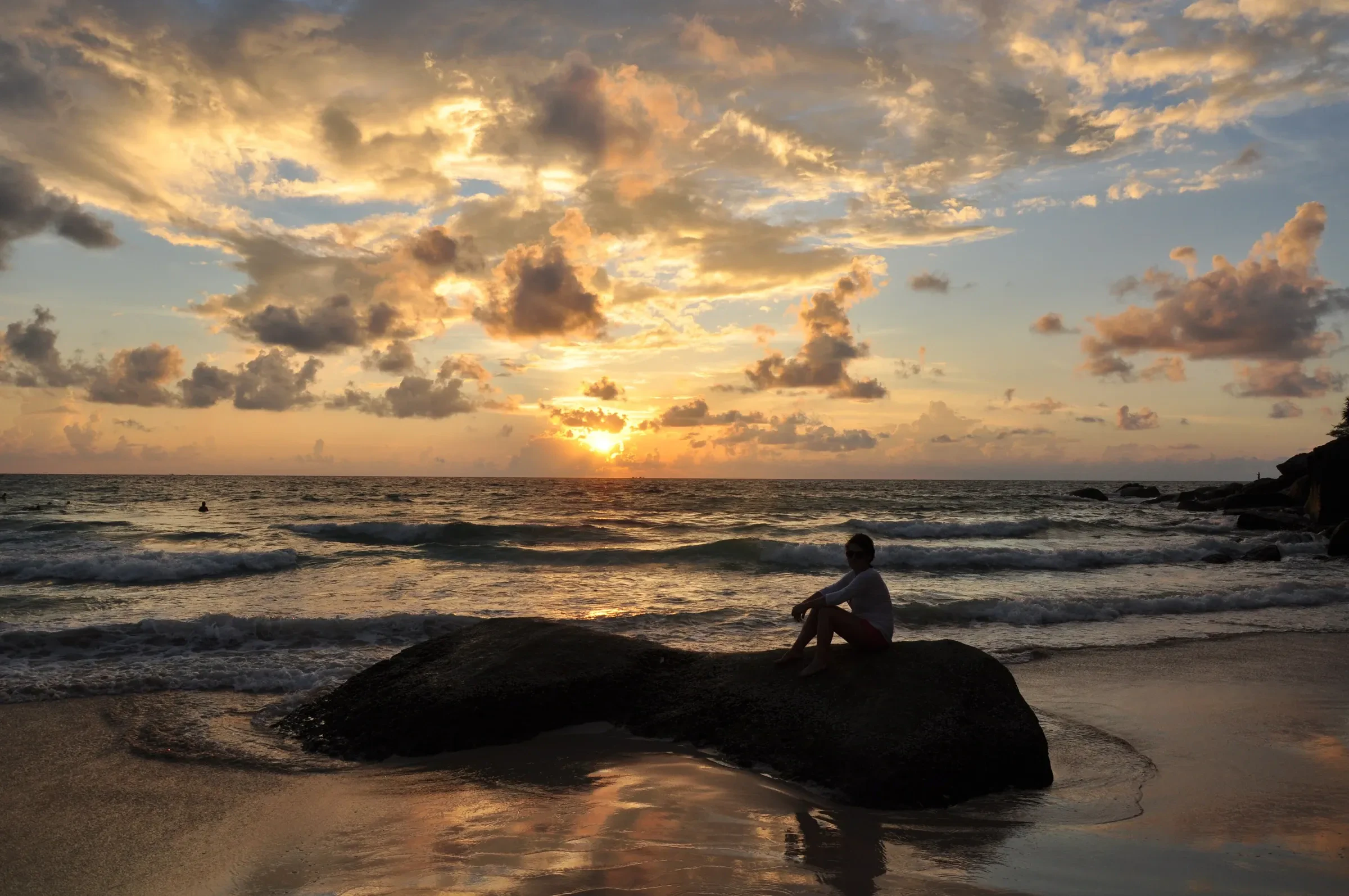 Sunset over the sea from Kata Noi beach with a person sitting on a rock