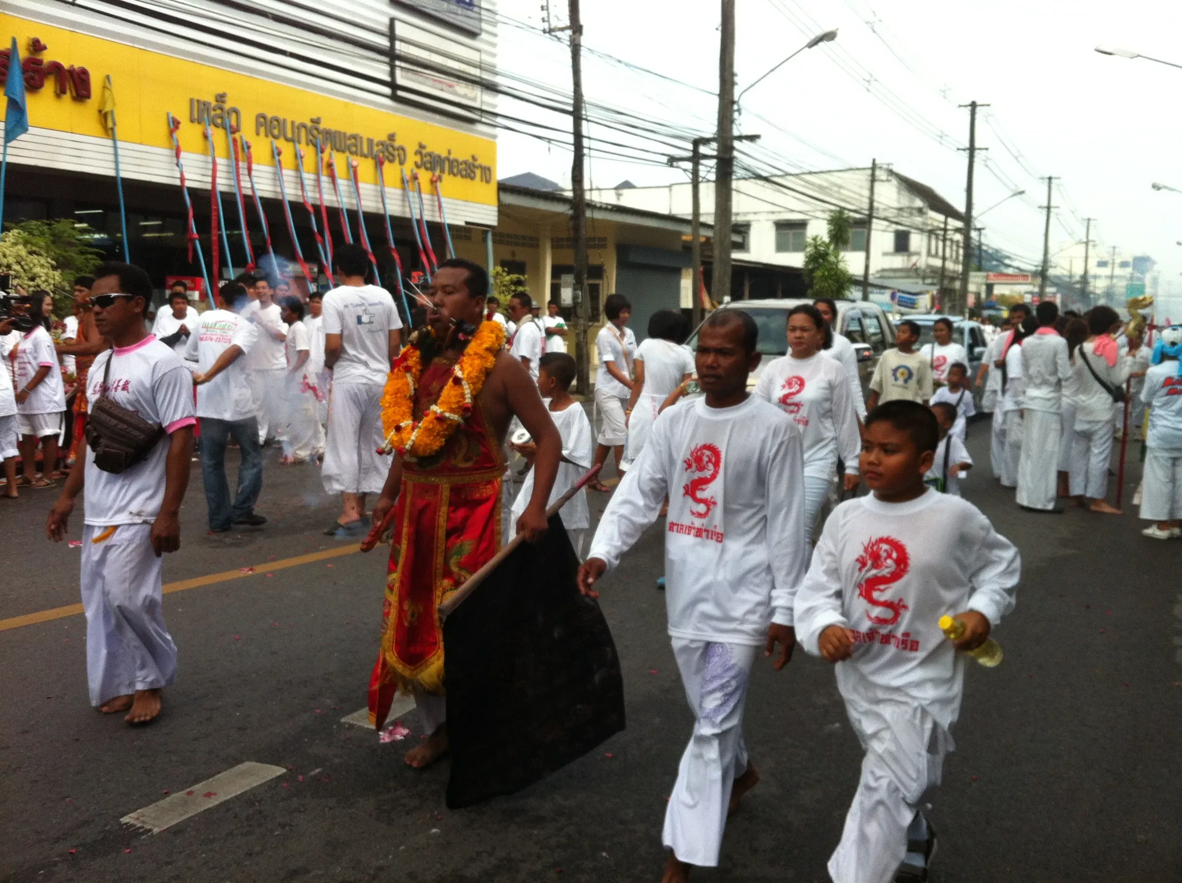 Devotees in white walking behind a medium in a morning procession through Phuket Town during the Vegetarian Festival