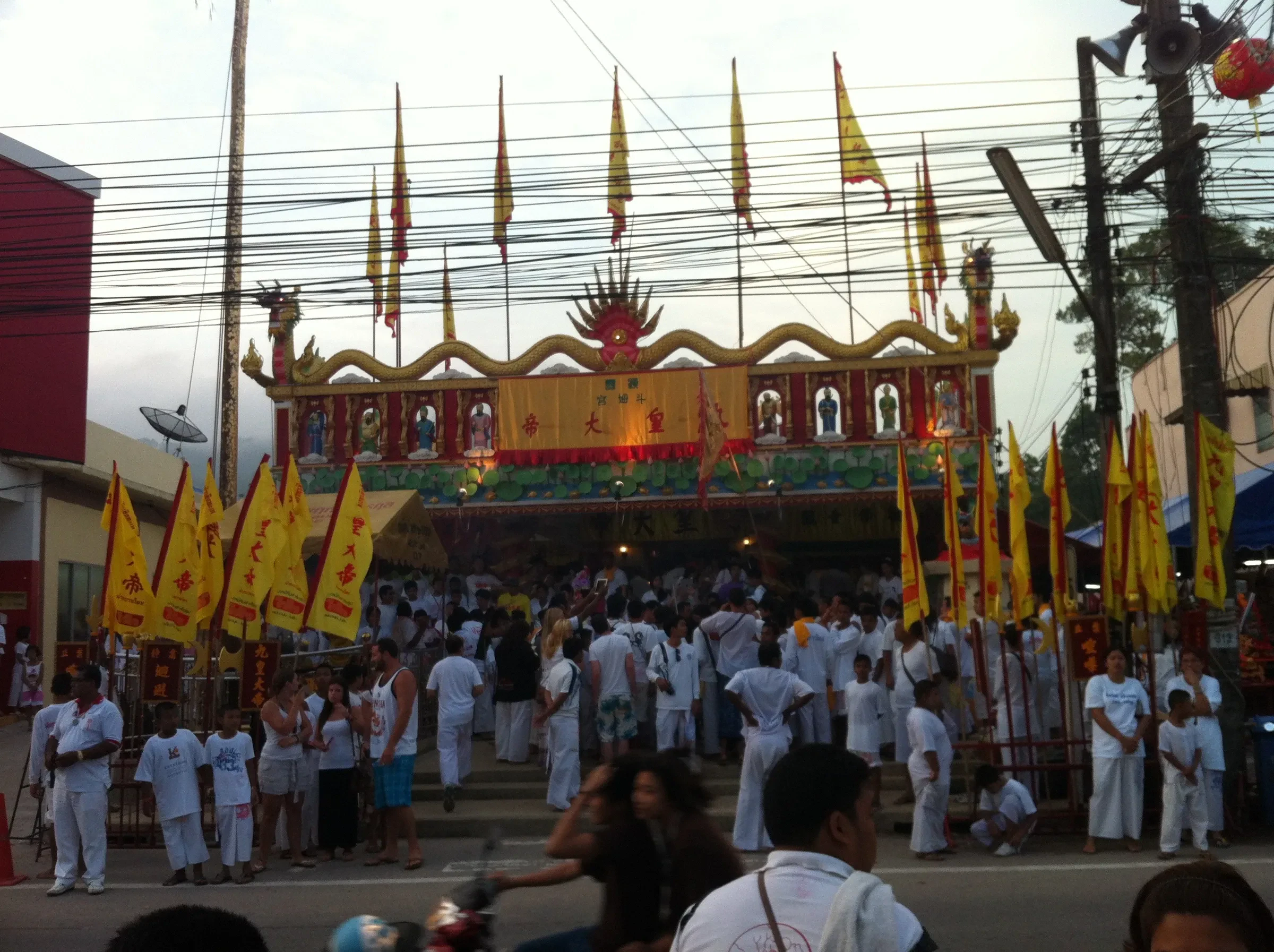 Devotees in white gathered outside a Chinese shrine hung with yellow flags in Cherngtalay, Phuket