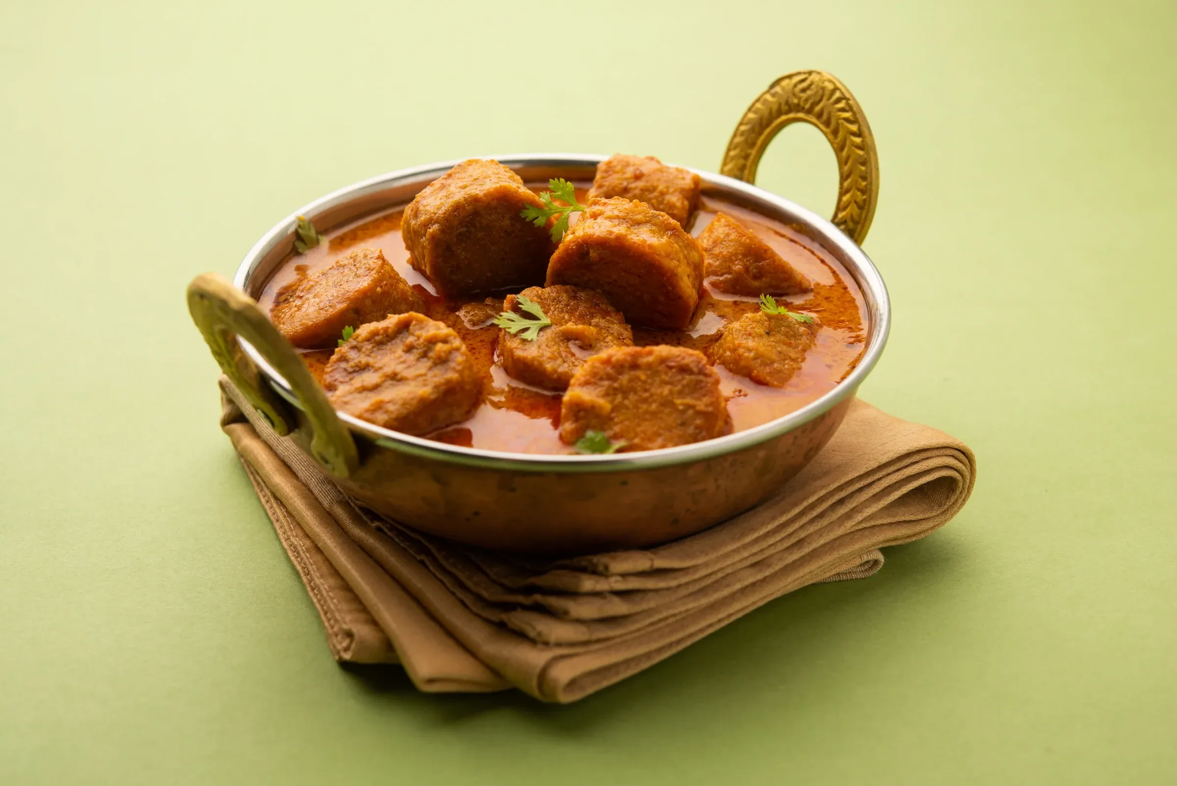 Gatte ki sabzi, gram flour dumplings in a spiced gravy, served in a brass kadai