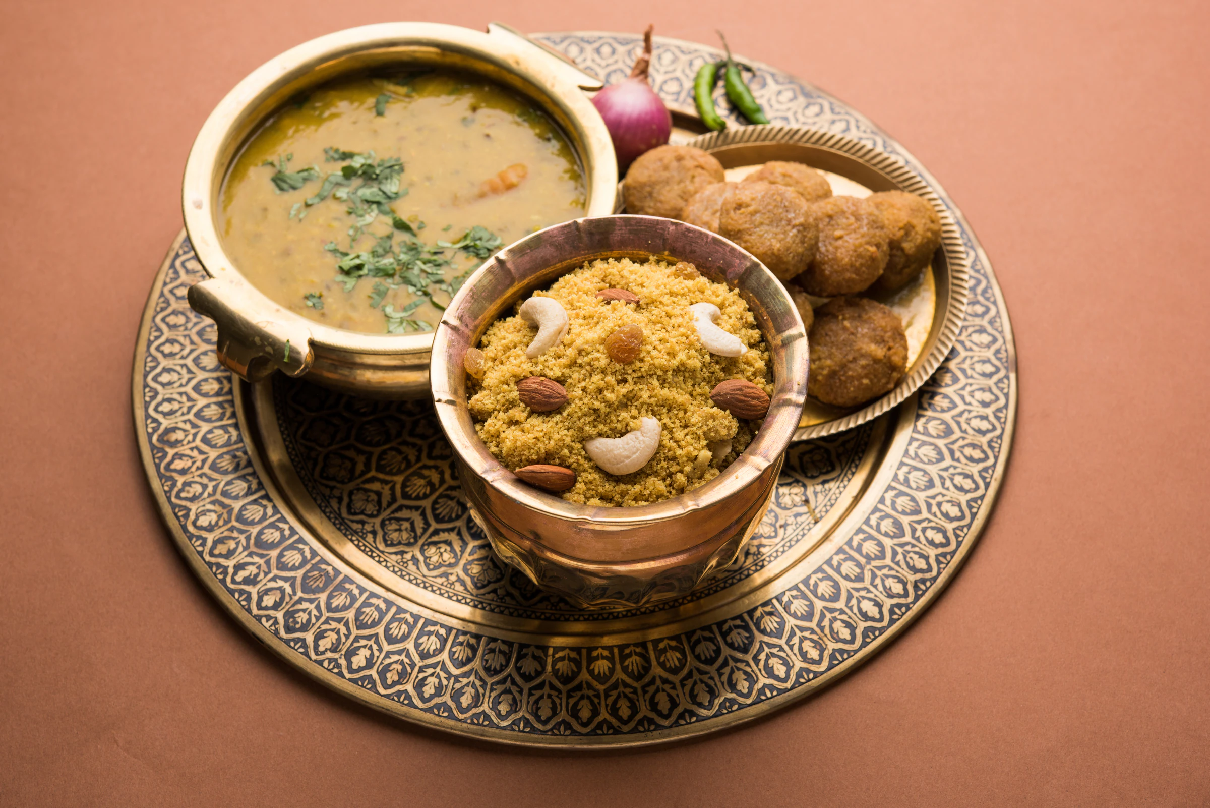 Dal baati churma served on an ornate brass plate, with lentil dal, sweet churma and baked wheat rolls