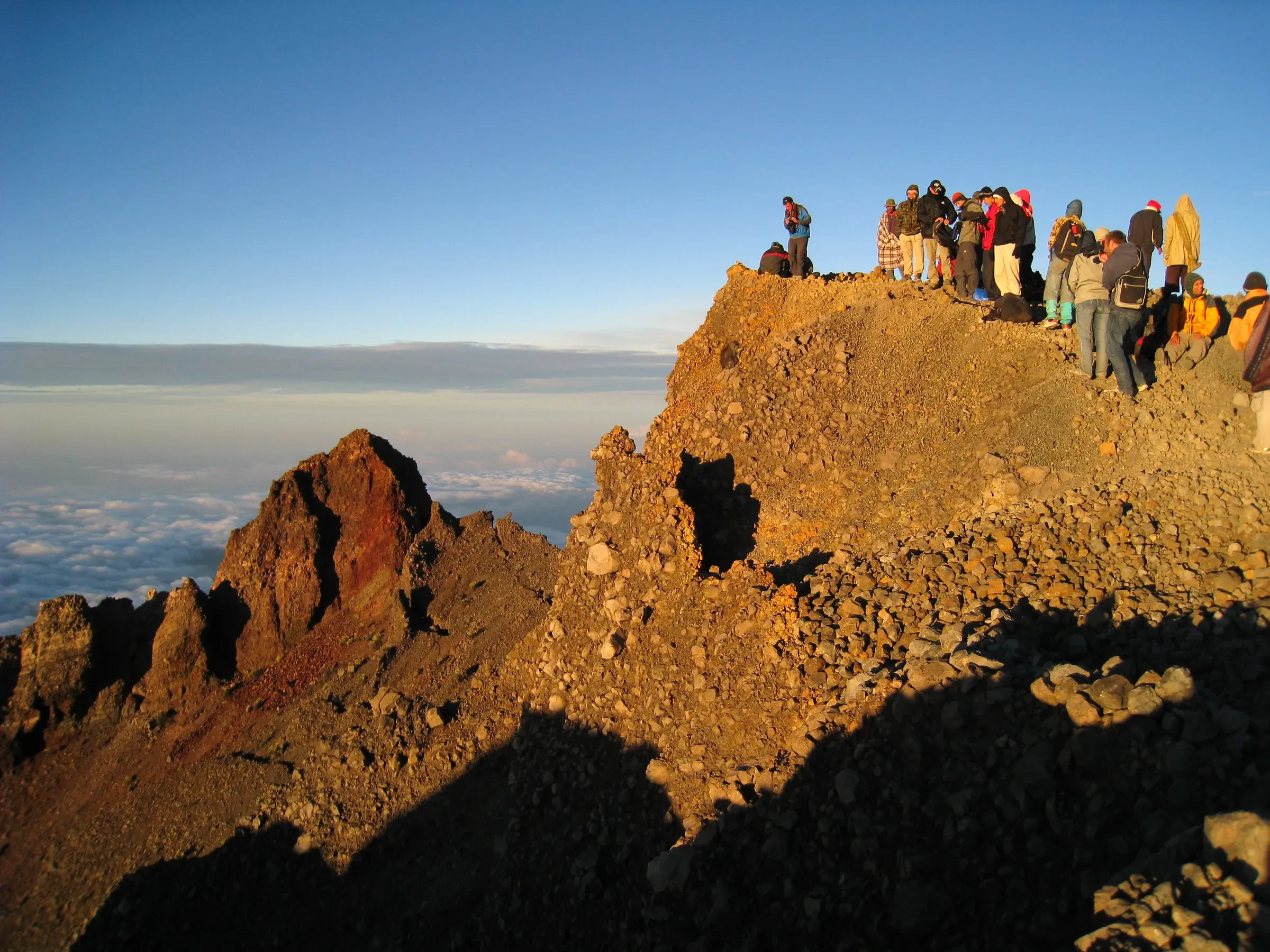 Climbers gathered on the rocky summit ridge of Rinjani at sunrise, with cloud far below