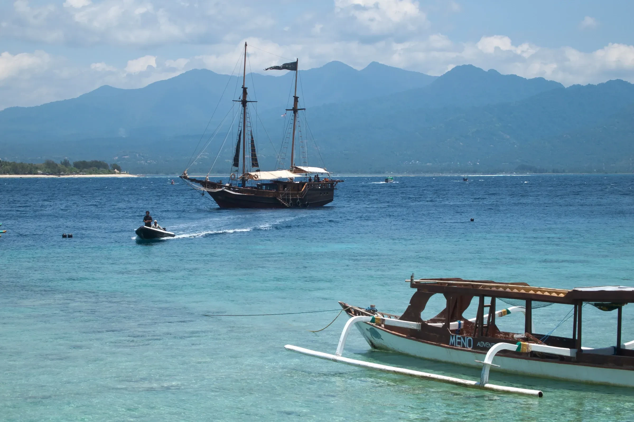 Lombok's coast and Mount Rinjani seen across the sea from Gili Meno, with boats in the water