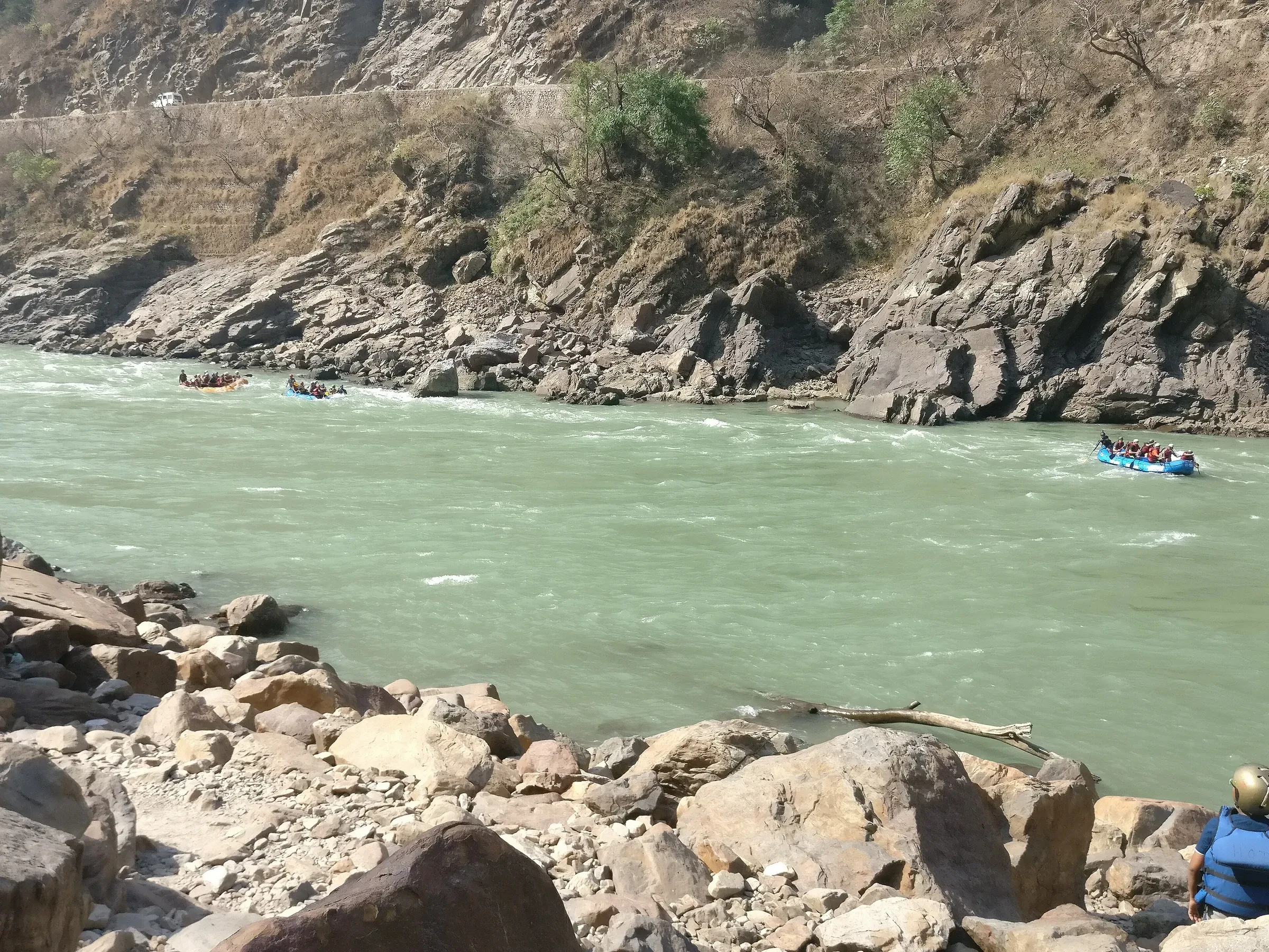 A raft on a rapid stretch of the green Ganga, seen from the rocky bank