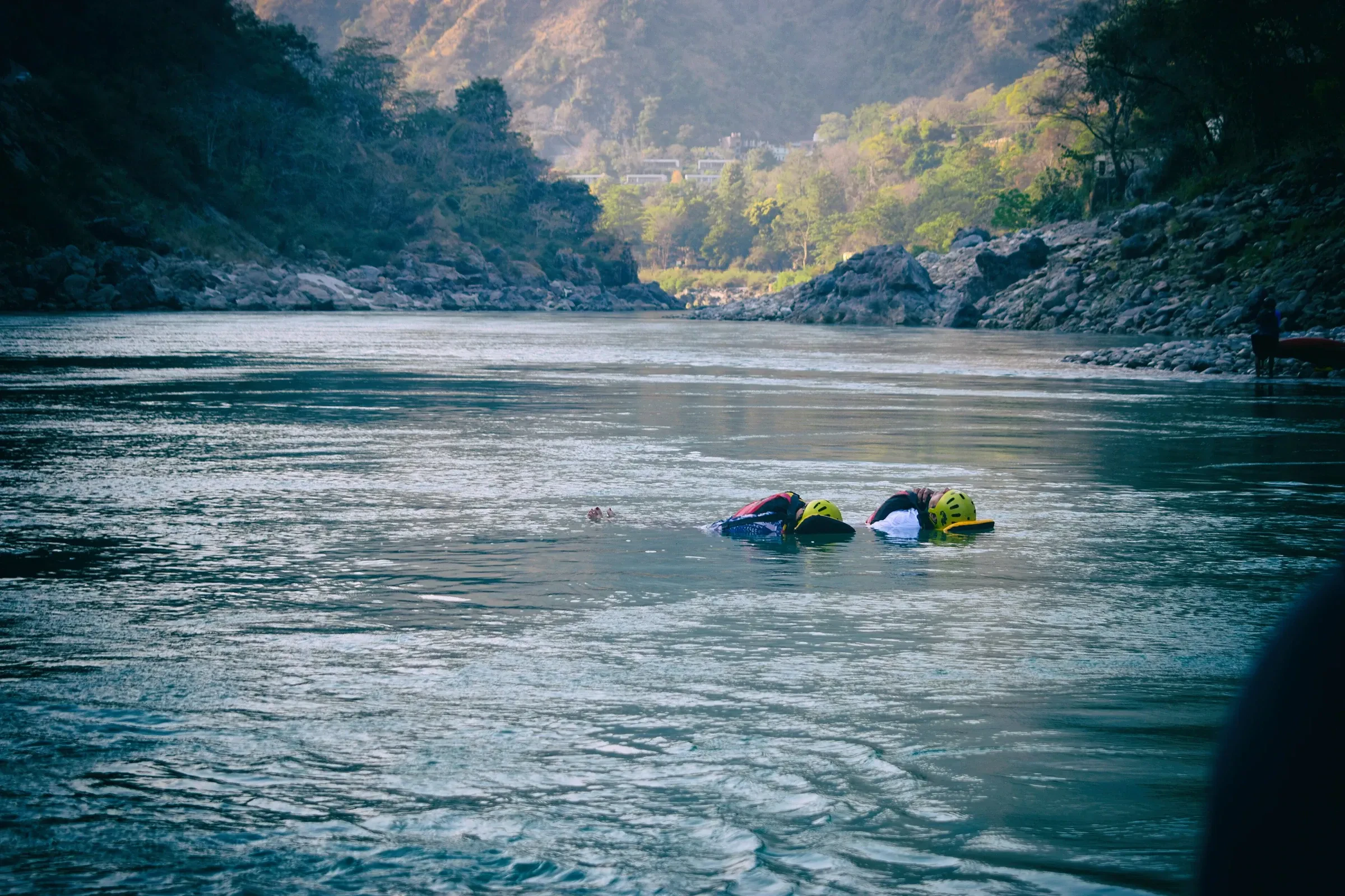 Two rafters in helmets and life jackets floating in a calm pool of the Ganga
