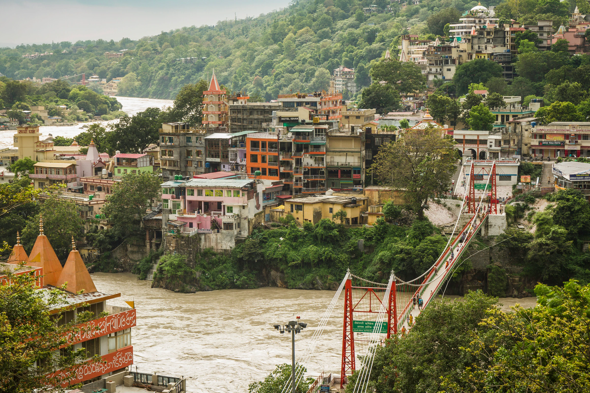 A suspension footbridge over the Ganga with the town of Rishikesh climbing the hillside