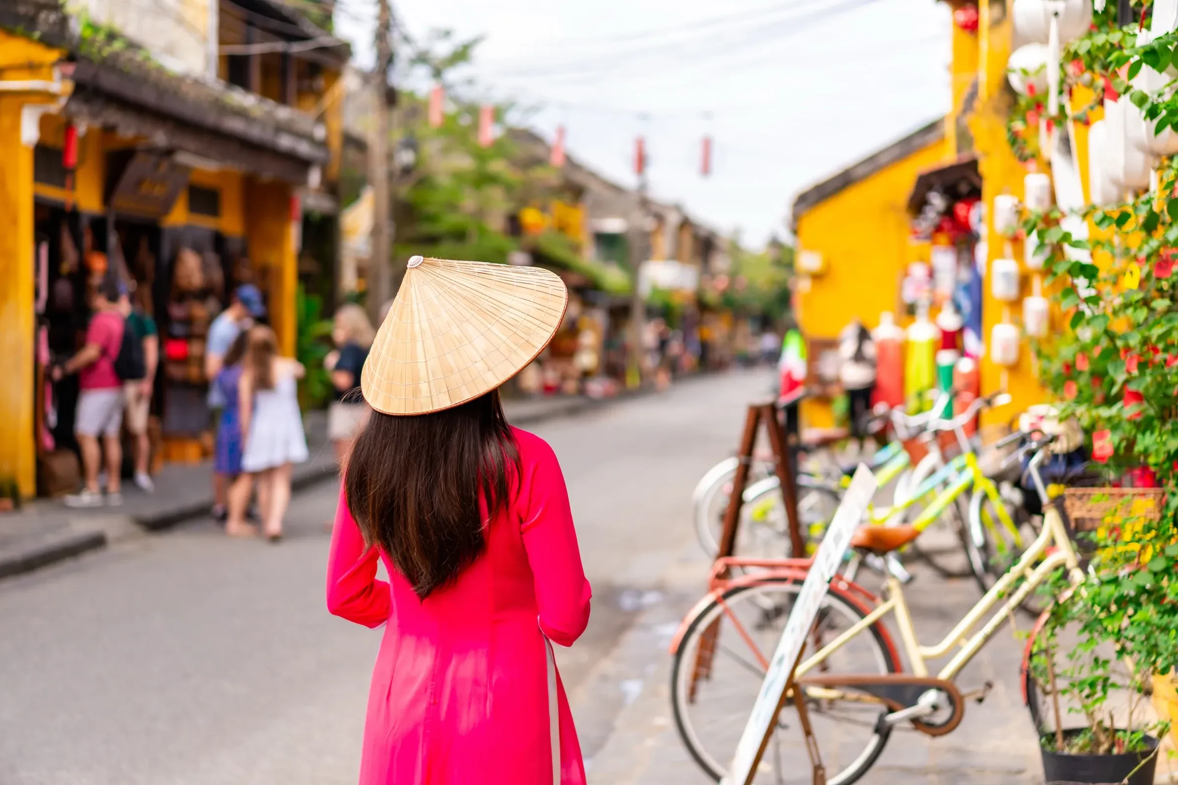 A woman in a conical hat and red dress walking along a street in Hoi An's old town, Vietnam