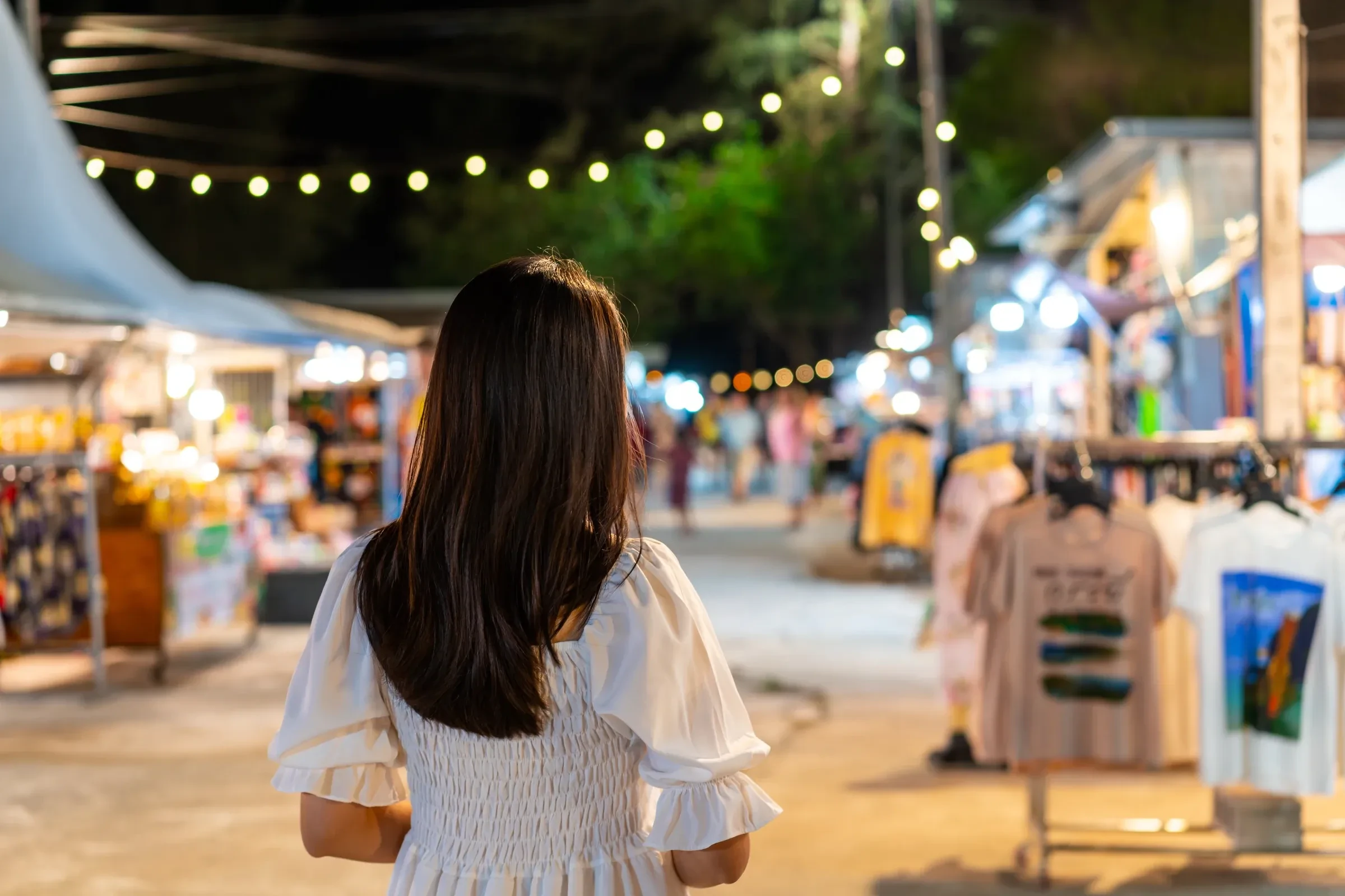 A woman walking through a night market in Thailand, seen from behind