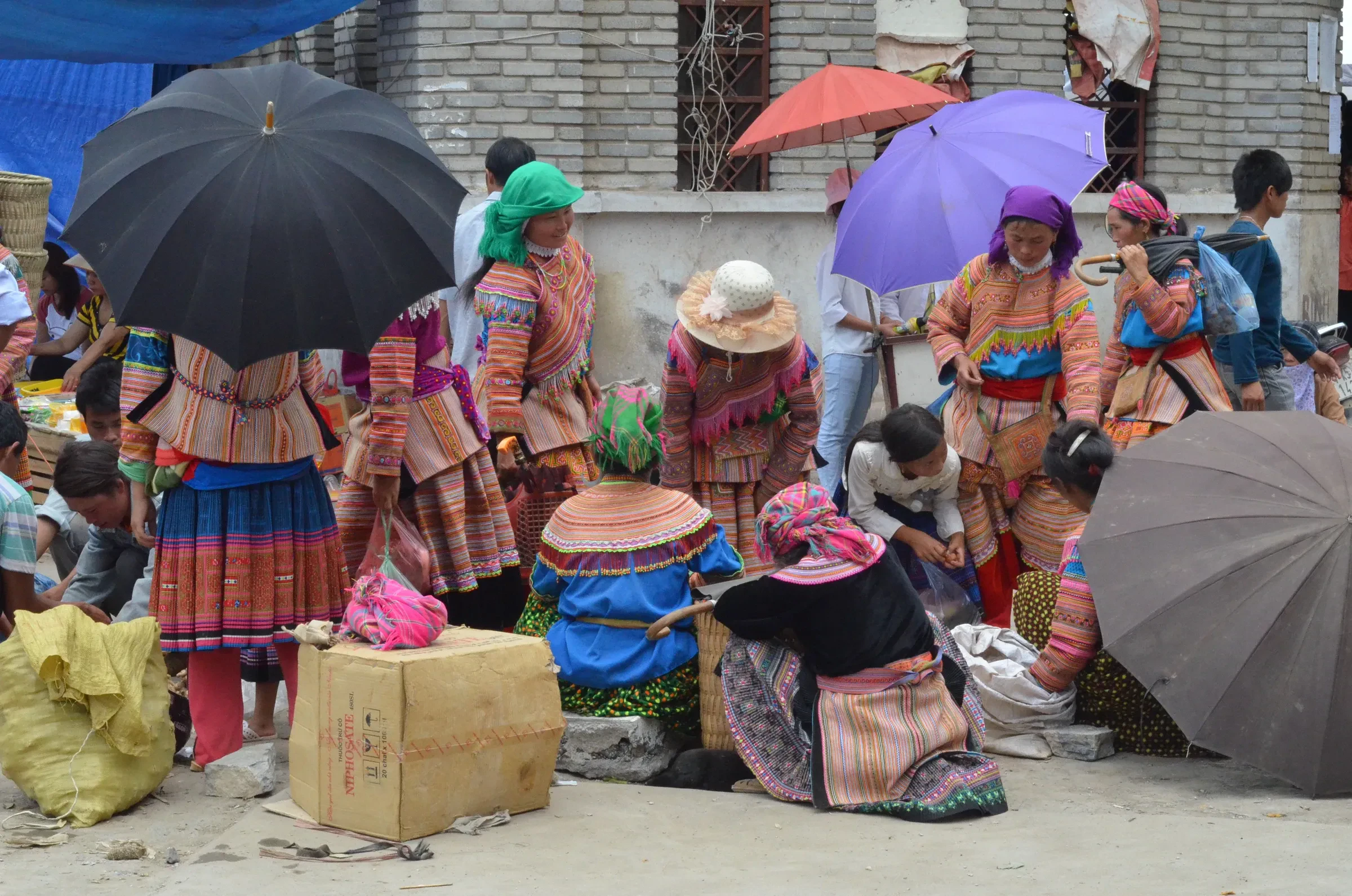 Traders in bright traditional clothes sitting under umbrellas at Bac Ha market