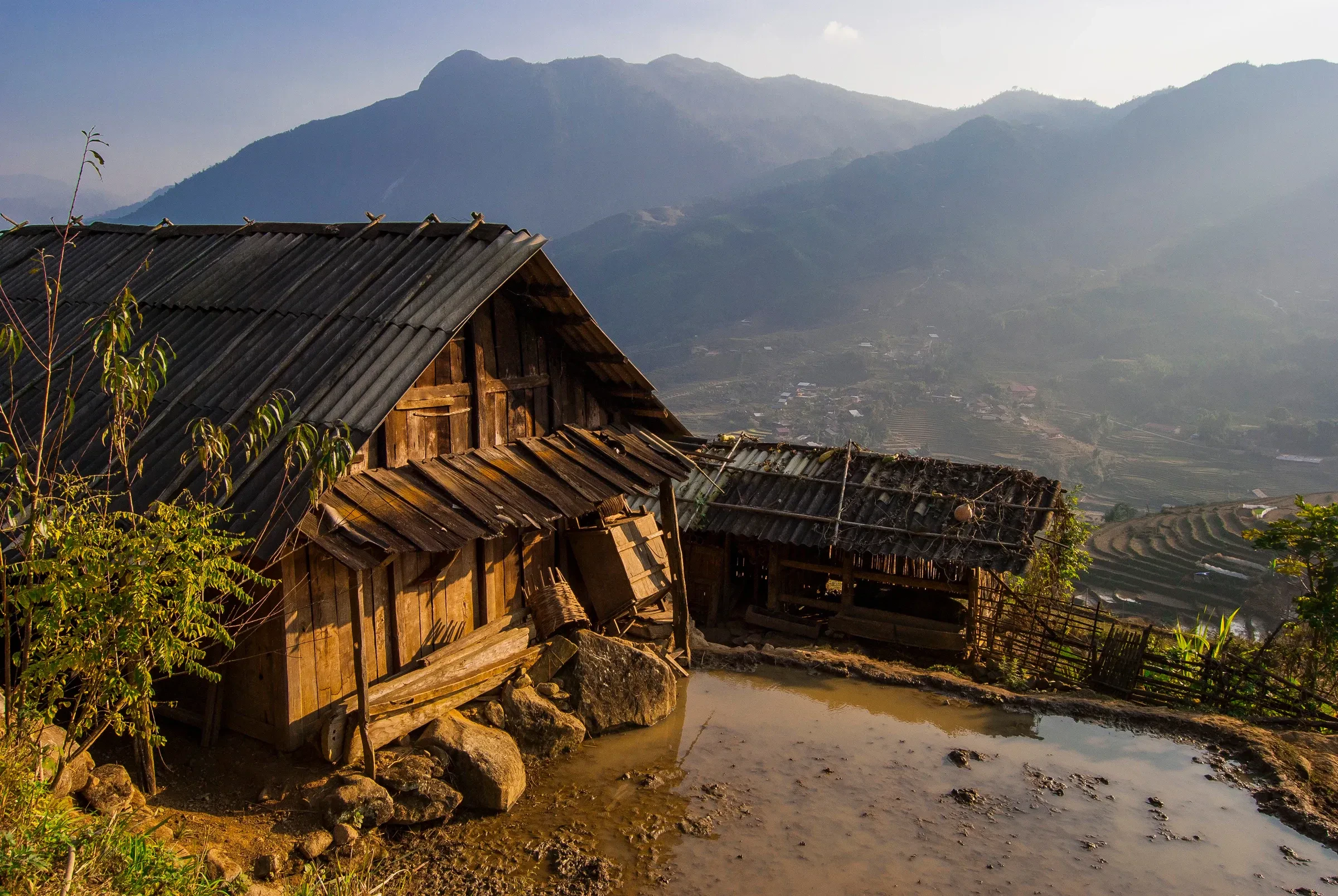 A weathered wooden house on a hillside above terraced fields in a mountain valley