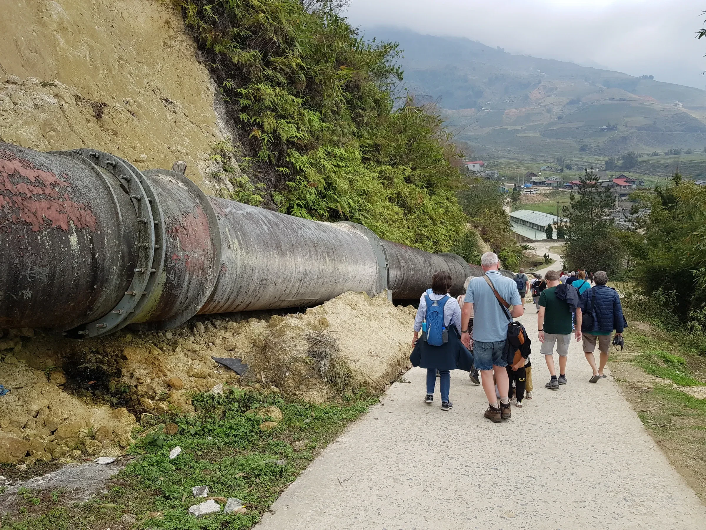 Trekkers walking along a concrete path beside a water pipe above the Muong Hoa valley near Ta Van