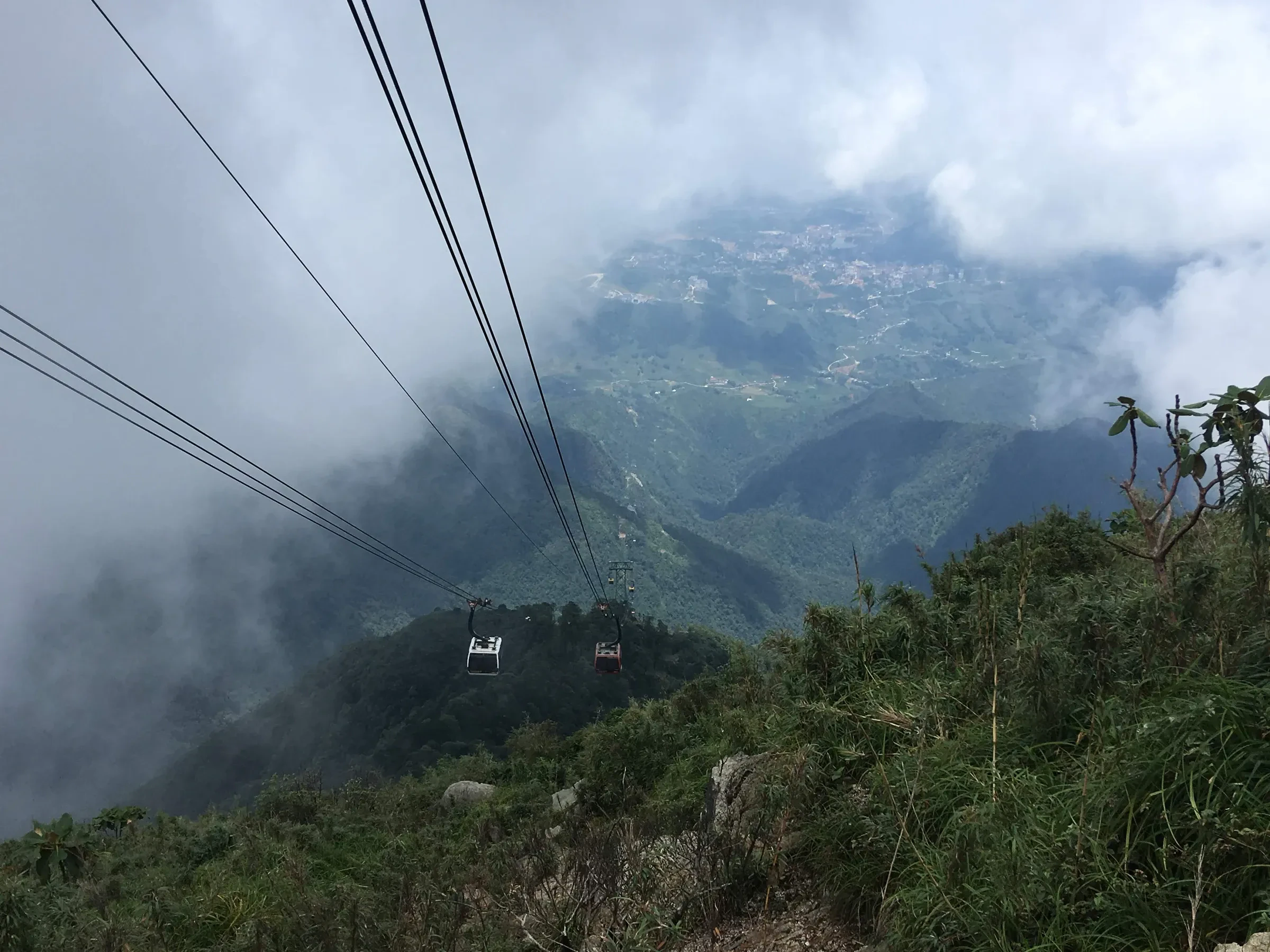 A Fansipan cable car crossing above cloud-filled mountain valleys, with the town of Sa Pa far below