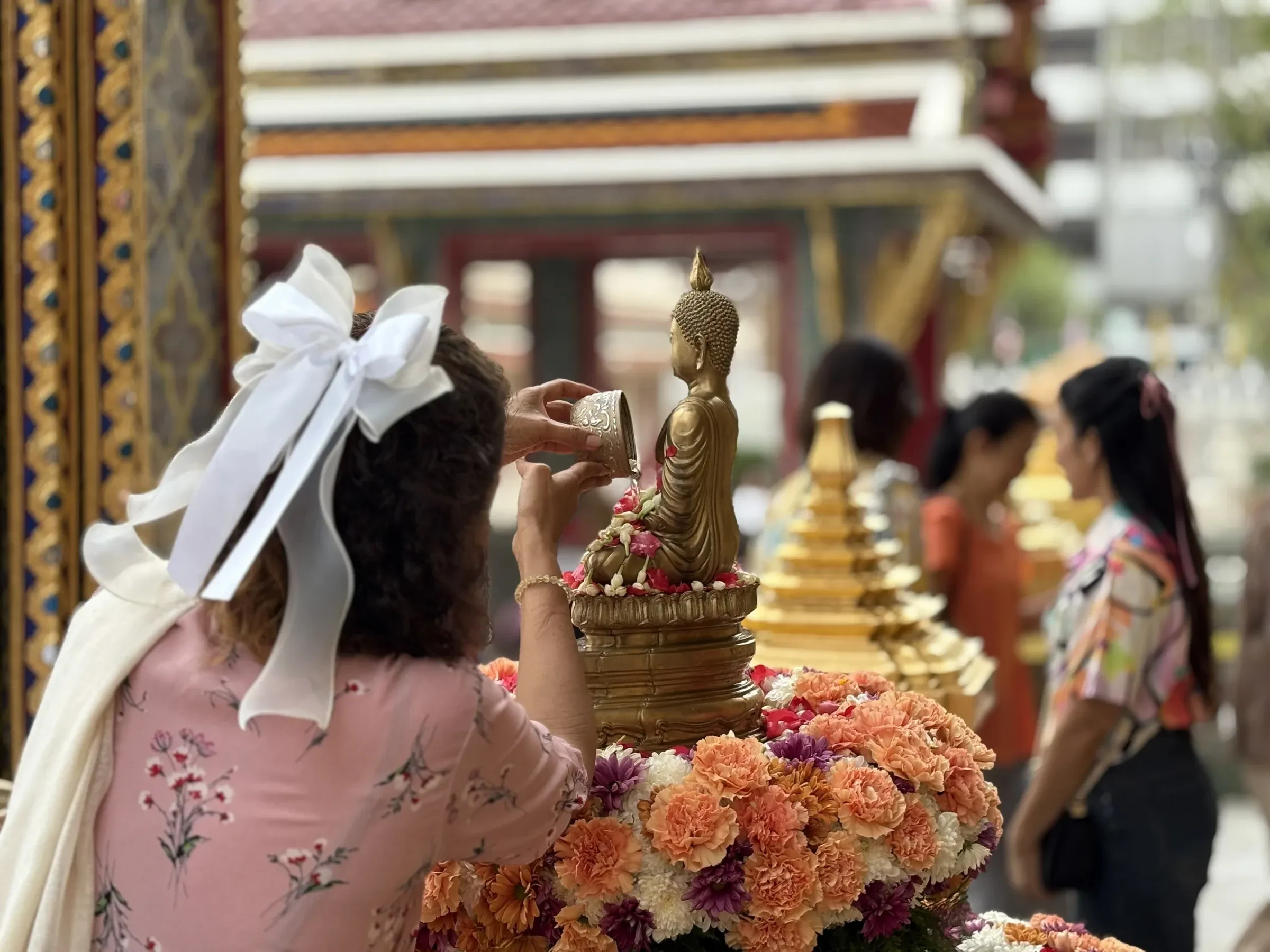 Scented water being poured over a golden Buddha image at a temple