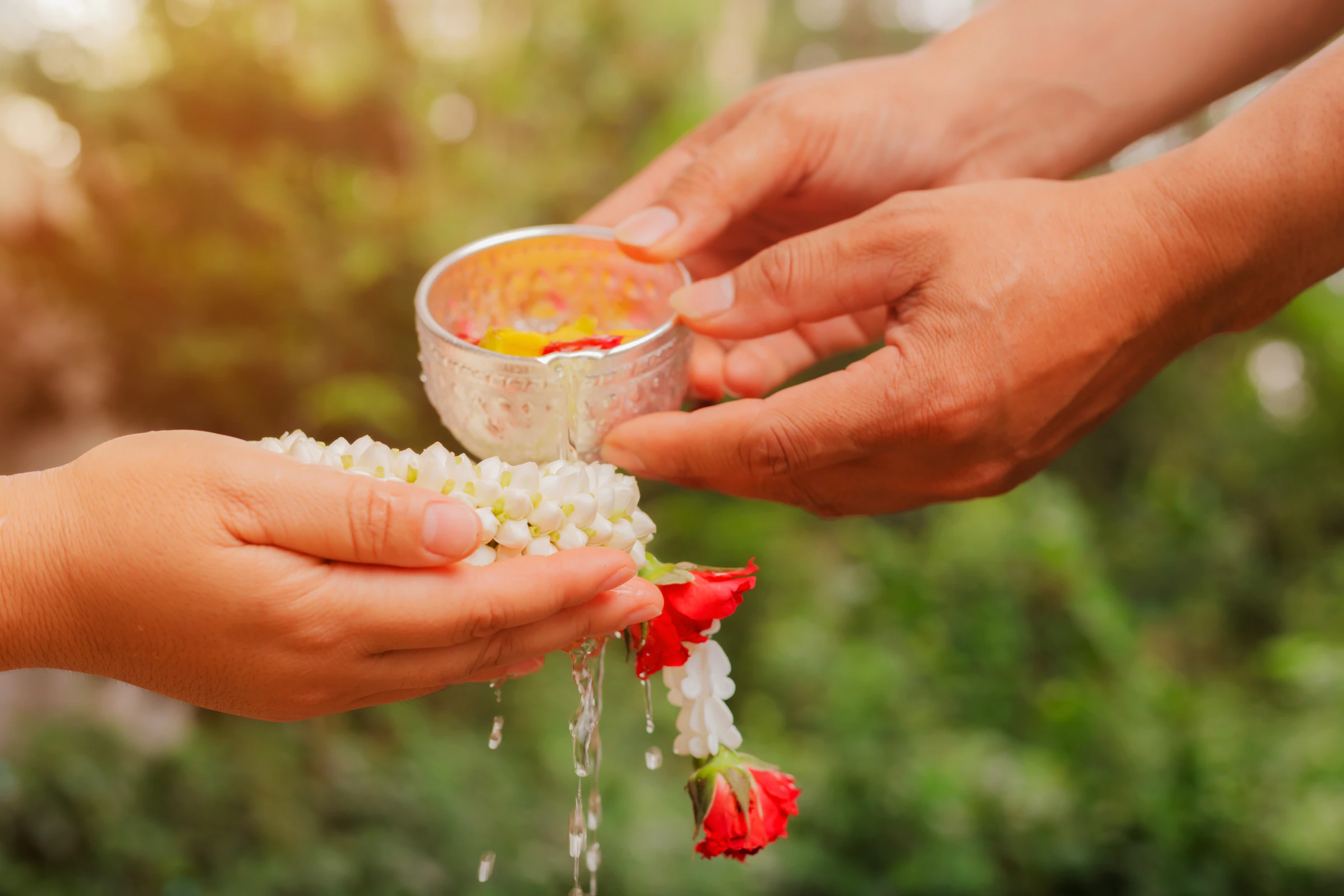 A young man pours water over an elder's hand and jasmine garland for rod nam dam hua