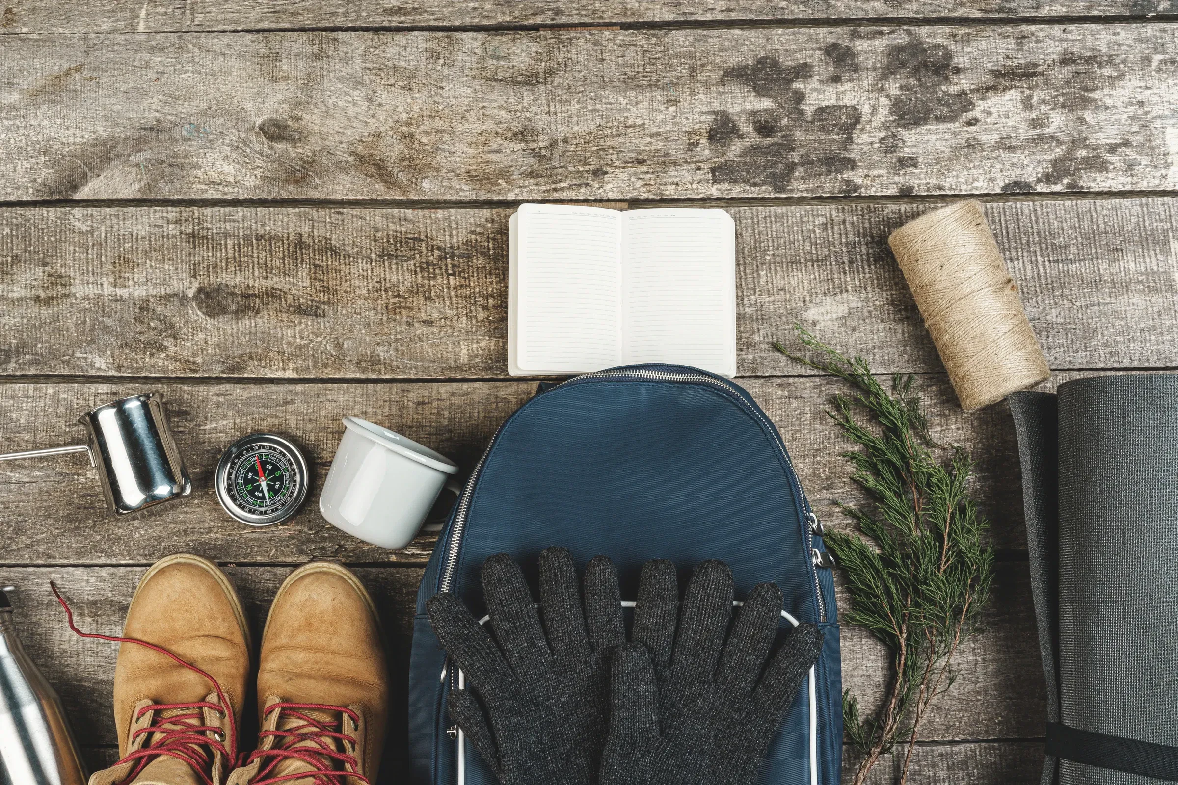 Hiking boots, a backpack, a compass and gloves laid out on a wooden floor