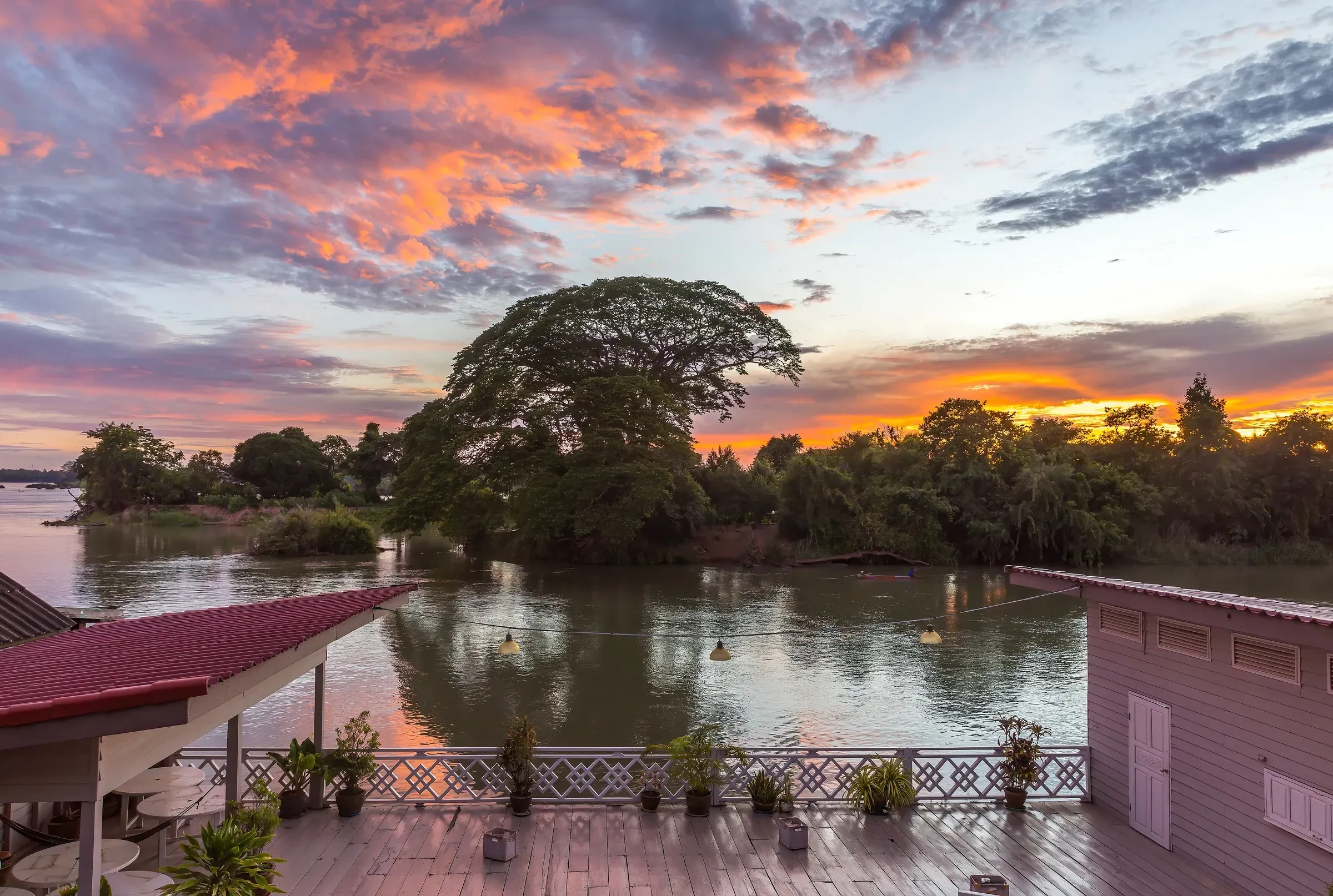Wooden terrace on the Mekong riverbank under an orange and pink sunrise sky, Si Phan Don