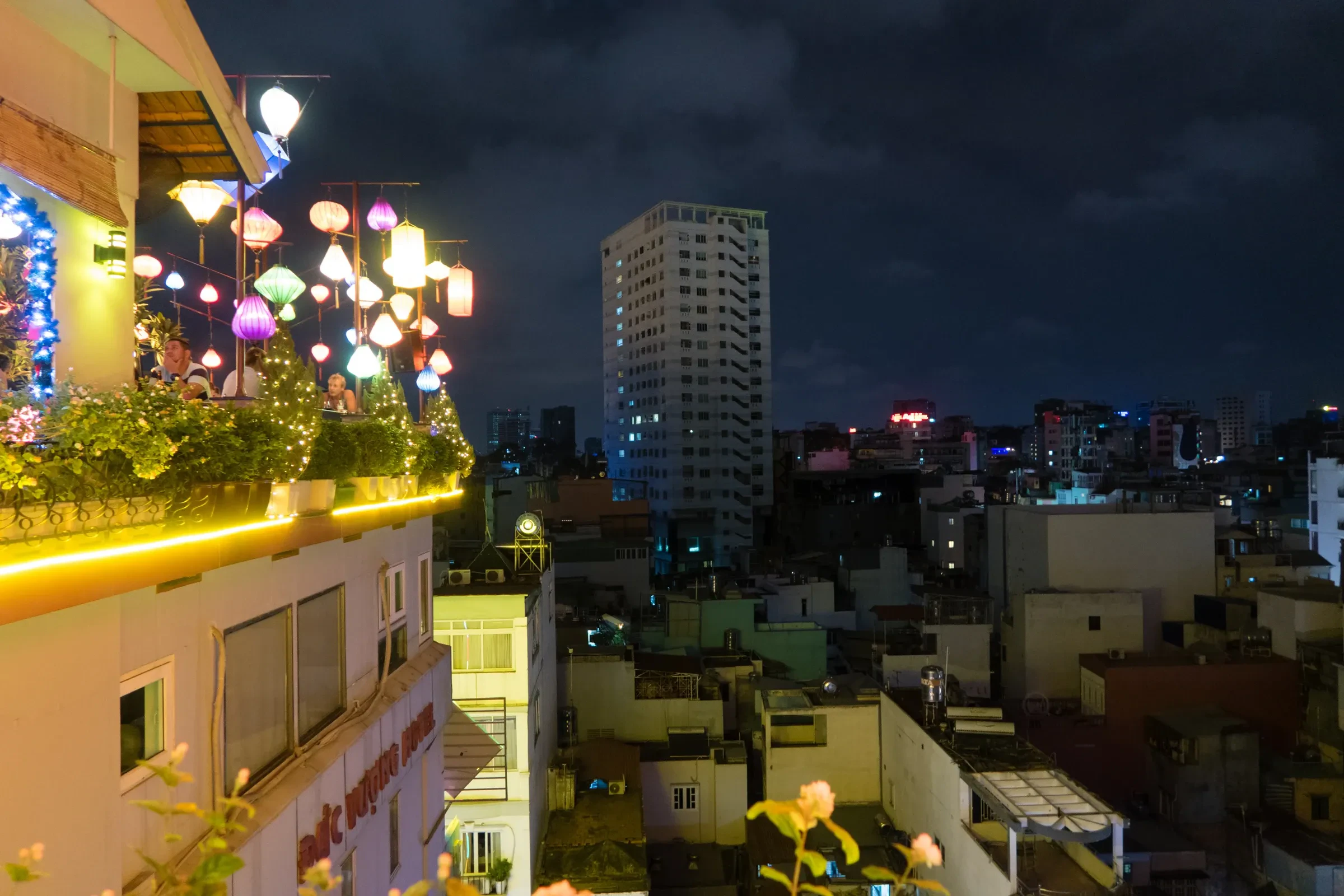 A terrace hung with lanterns above Bui Vien in Ho Chi Minh City at night, with rooftops and a tower beyond