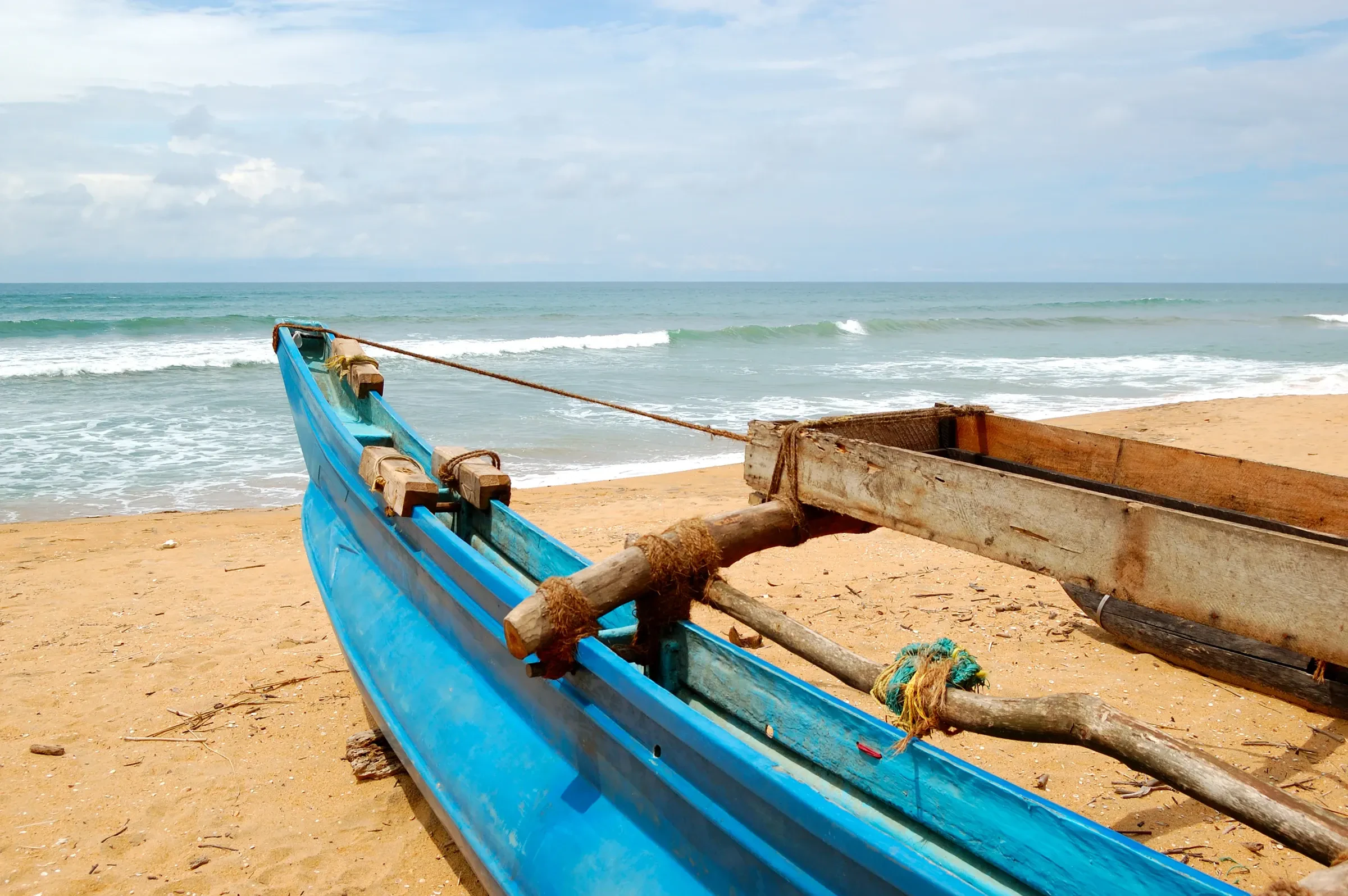 A blue wooden outrigger fishing boat pulled up on a Sri Lankan beach