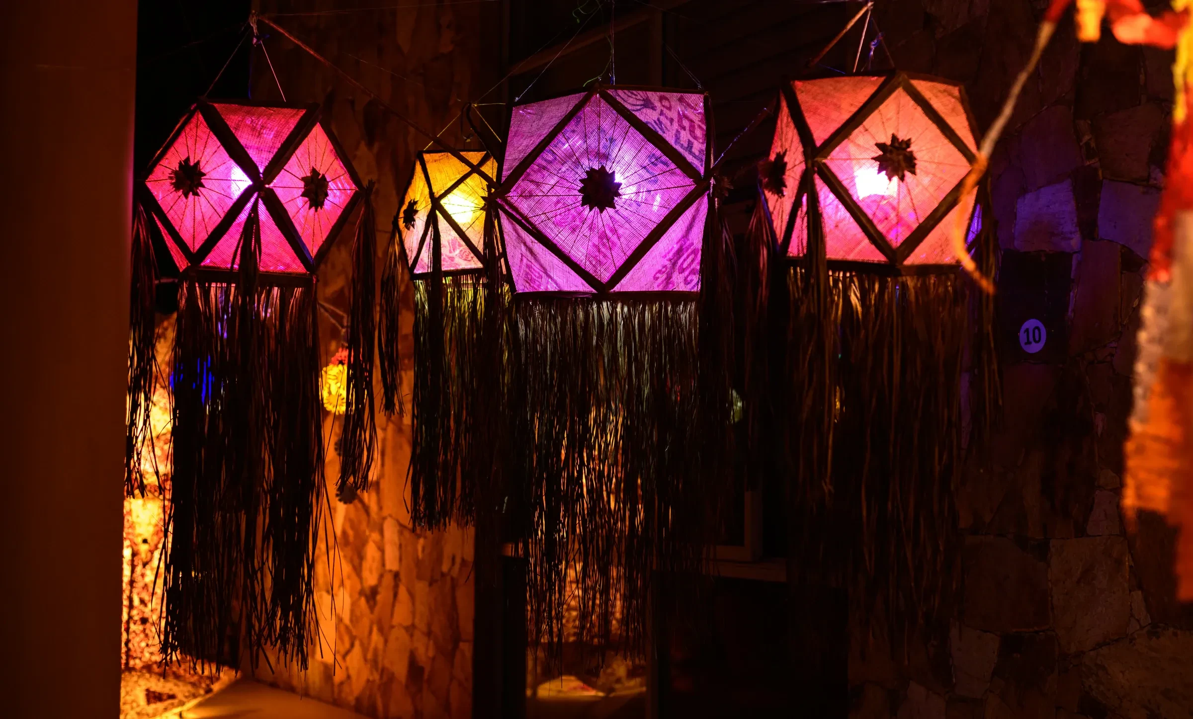 Glowing paper Vesak lanterns hanging in pink, purple and orange