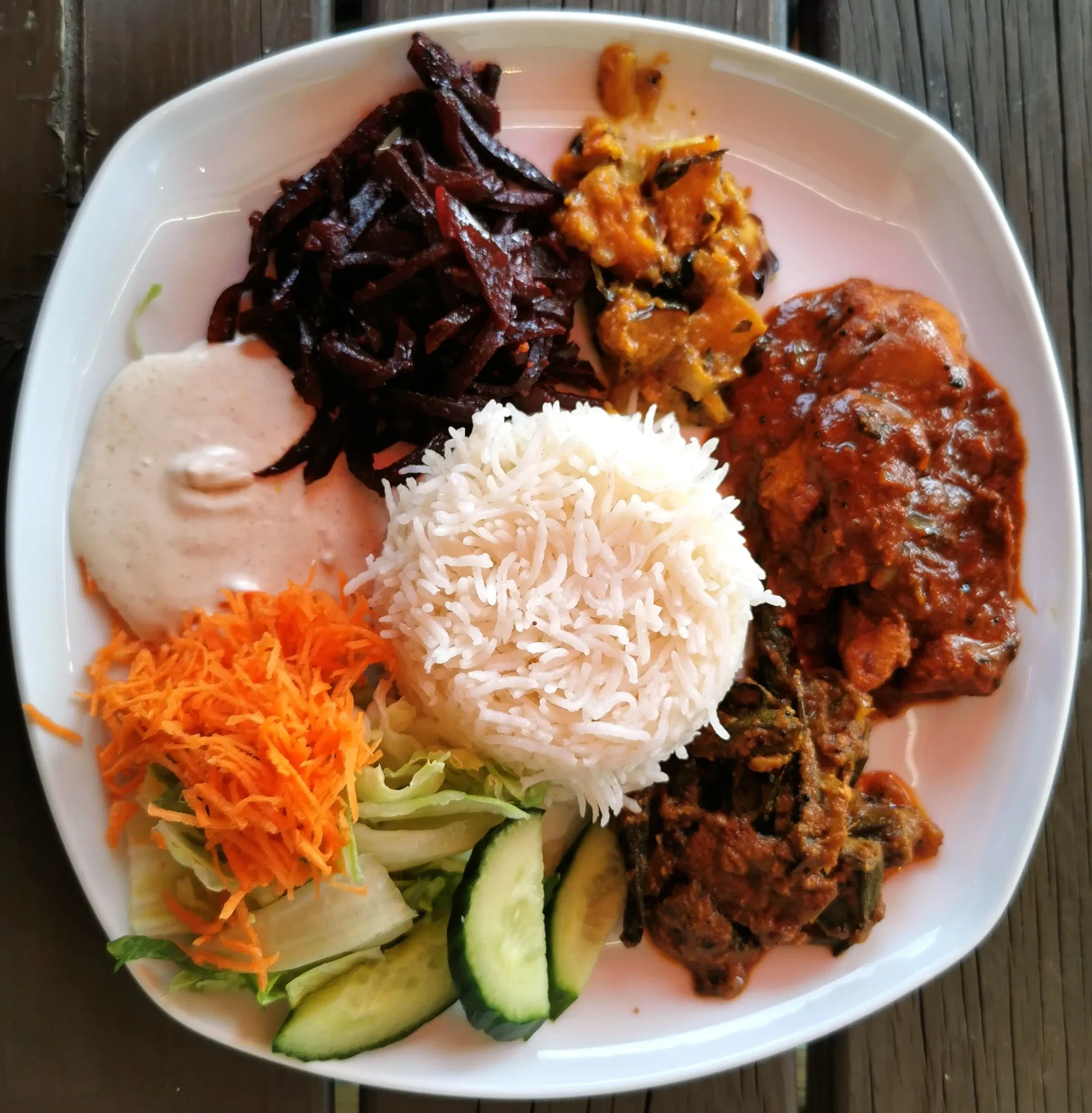 A plate of Sri Lankan rice and curry with beetroot curry, carrot and cucumber