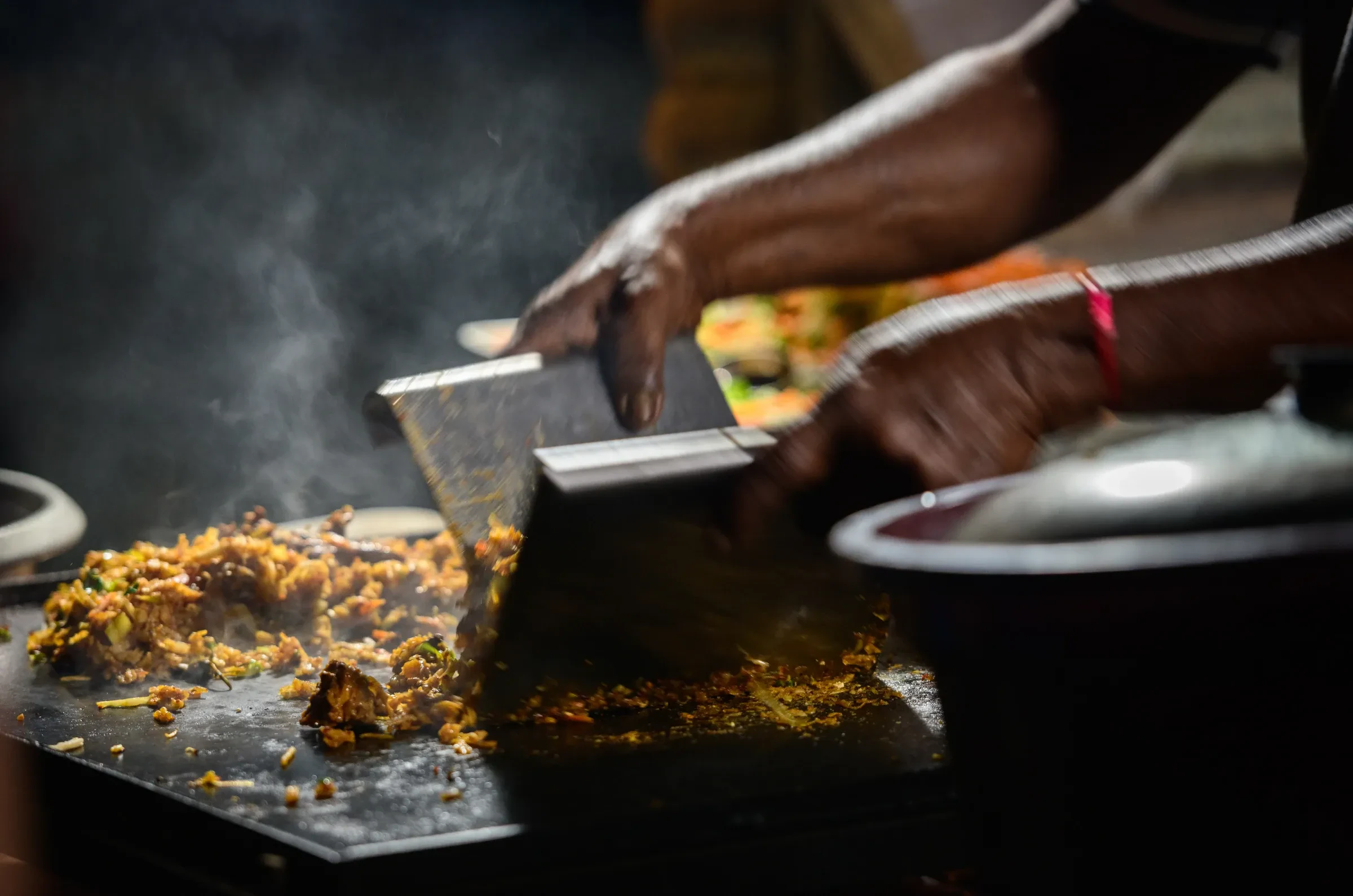 A kottu roti vendor chopping kottu on a hot steel griddle