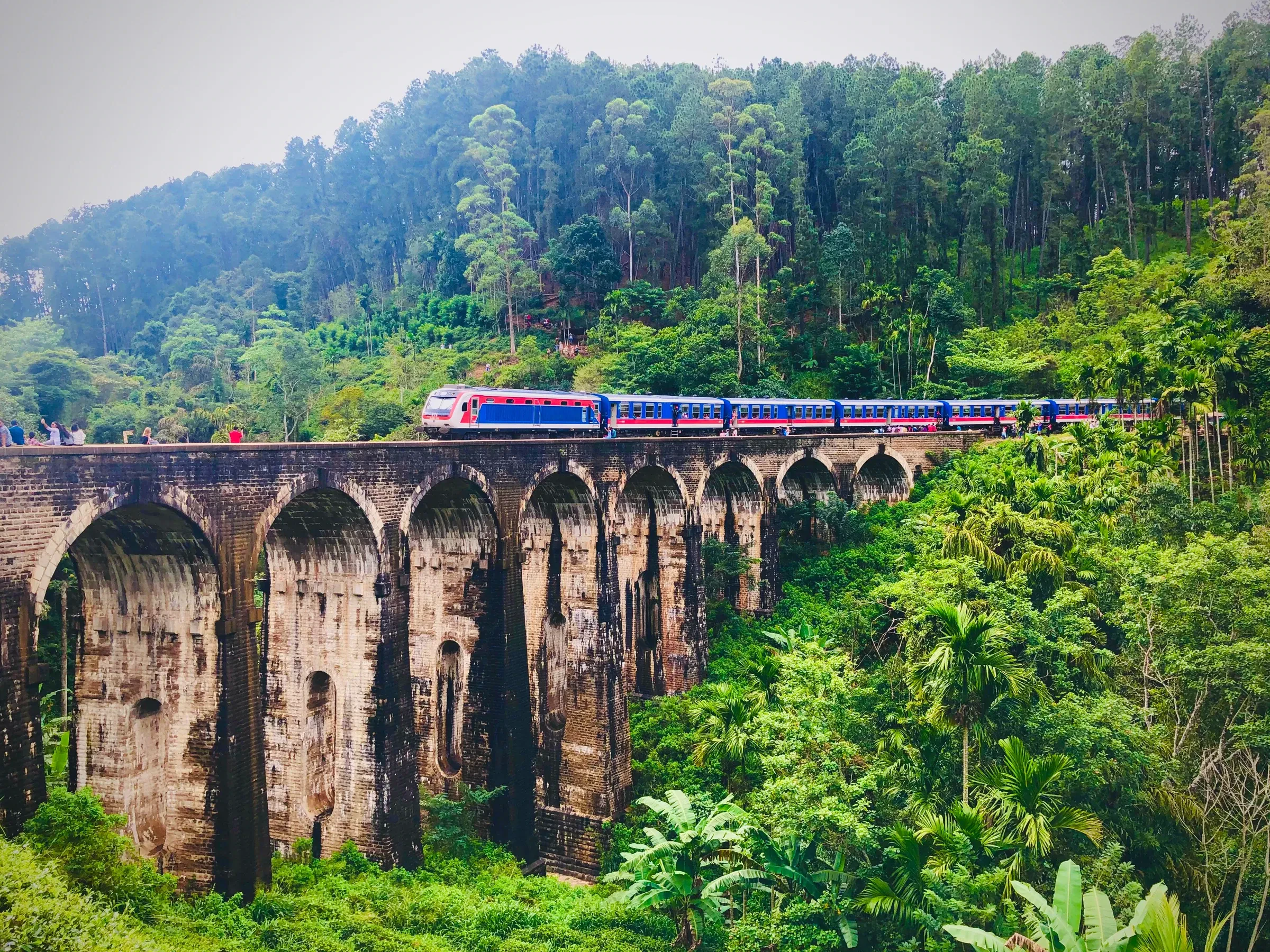 A passenger train crossing the Nine Arches Bridge near Ella, surrounded by forest