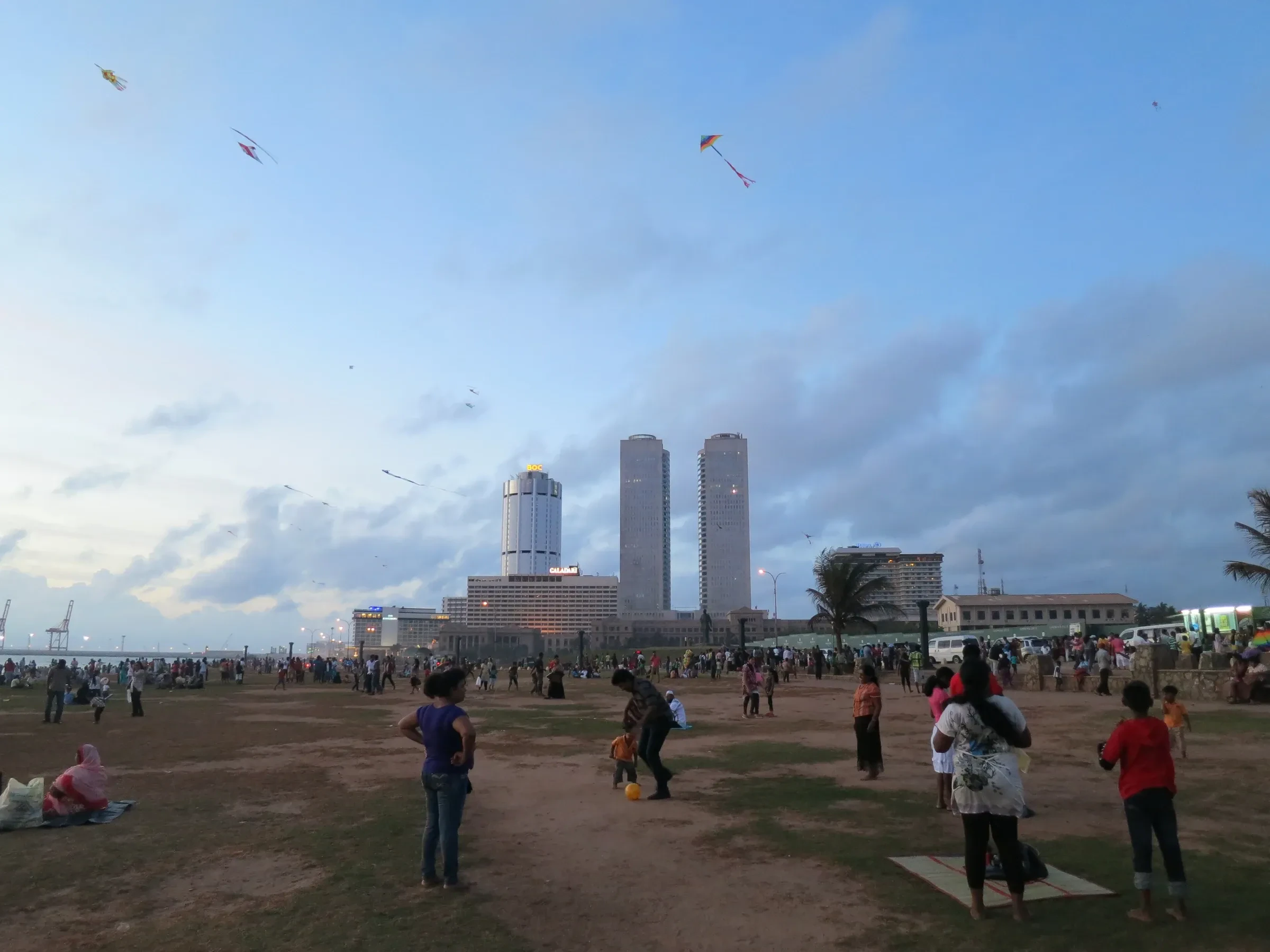 People on Galle Face Green in Colombo, with kites in the sky and city towers behind
