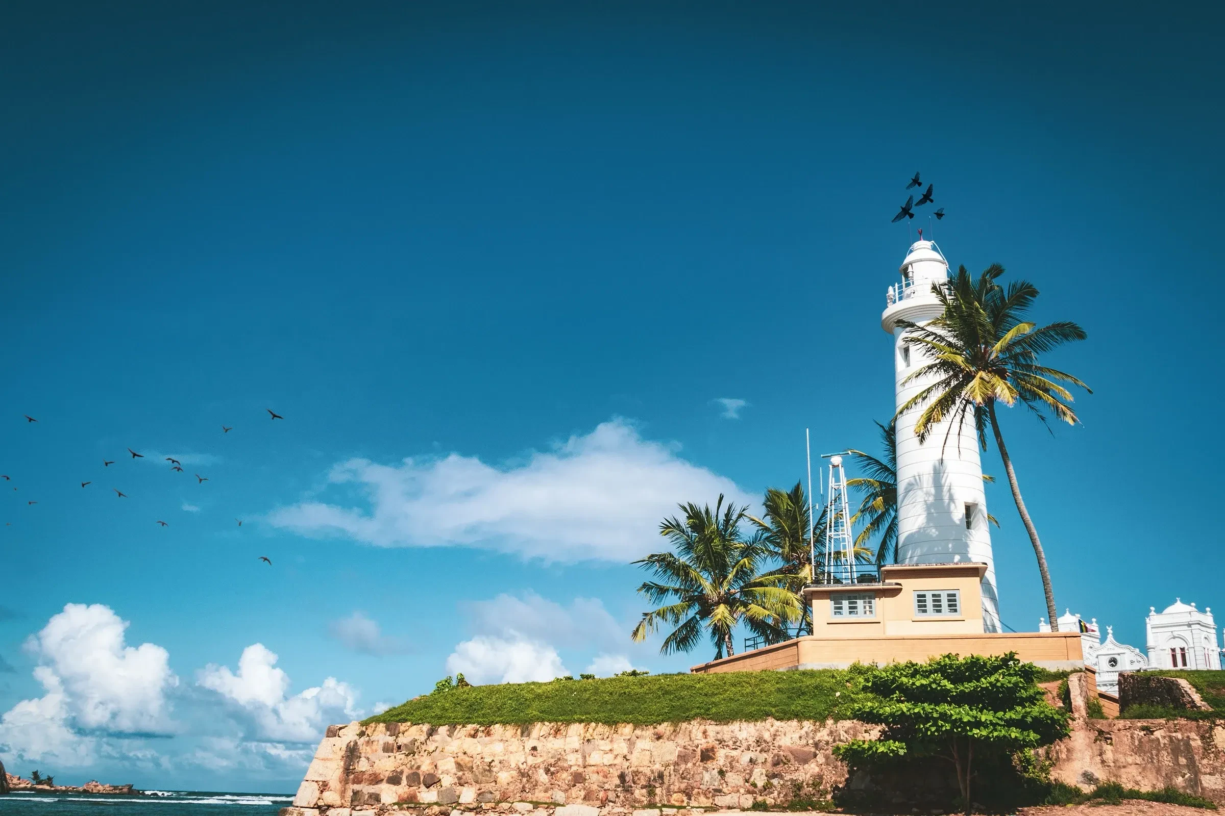 The Galle Fort lighthouse above the fort wall, with palm trees and the sea