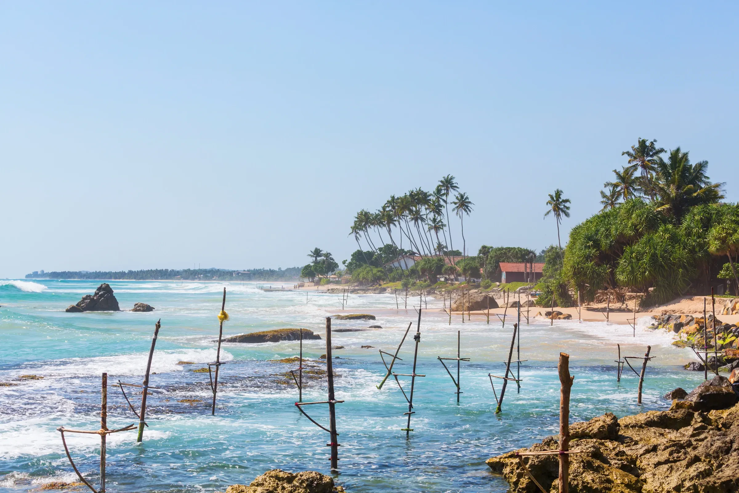 Waves breaking over rocks on a Sri Lankan beach lined with fishing stilts