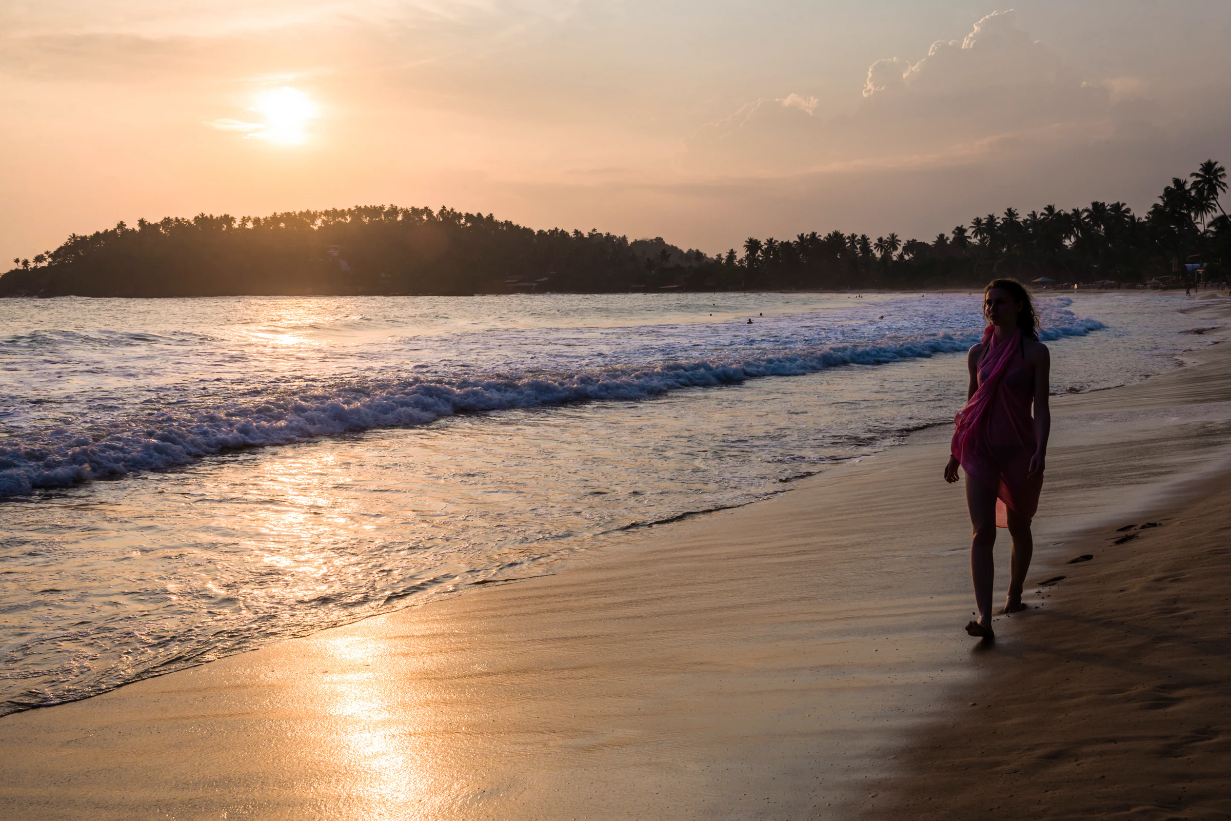 A woman walking along the shore of a Sri Lankan beach at sunset