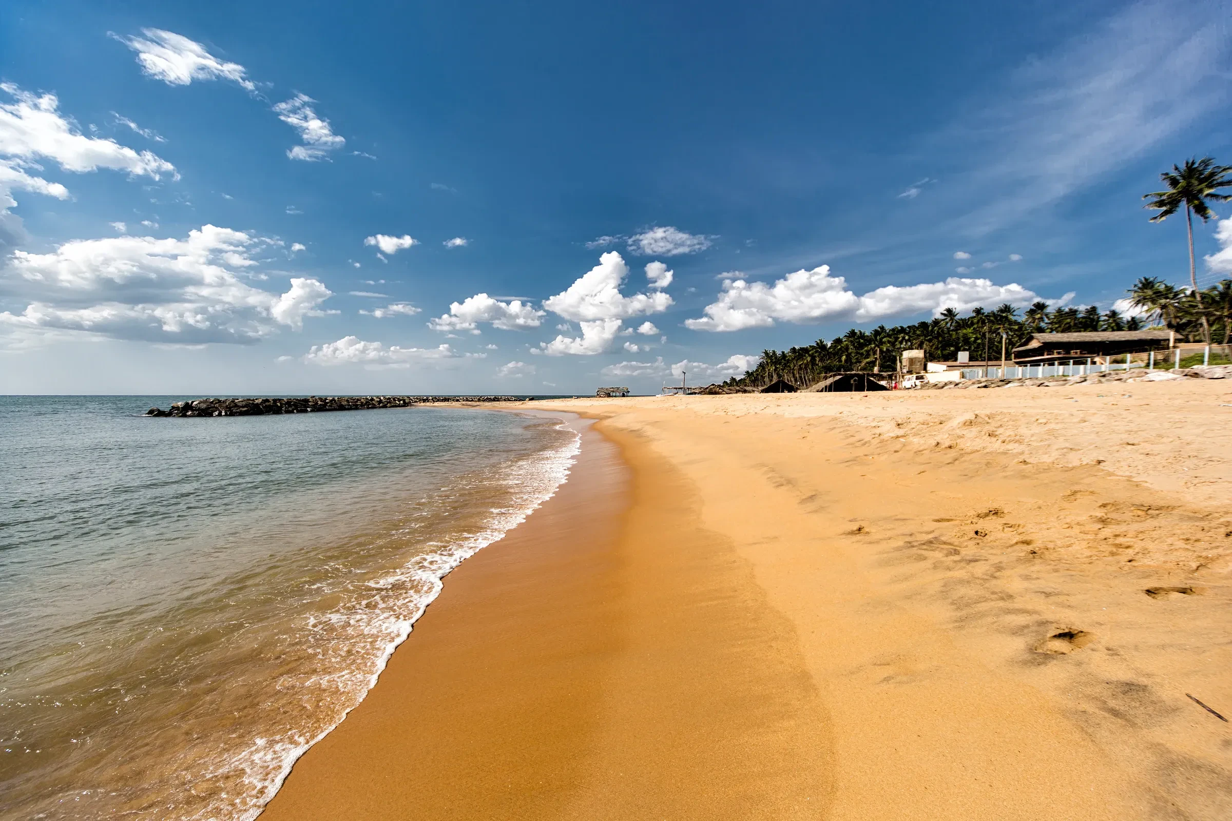 Negombo's sandy beach with waves rolling in under a blue sky