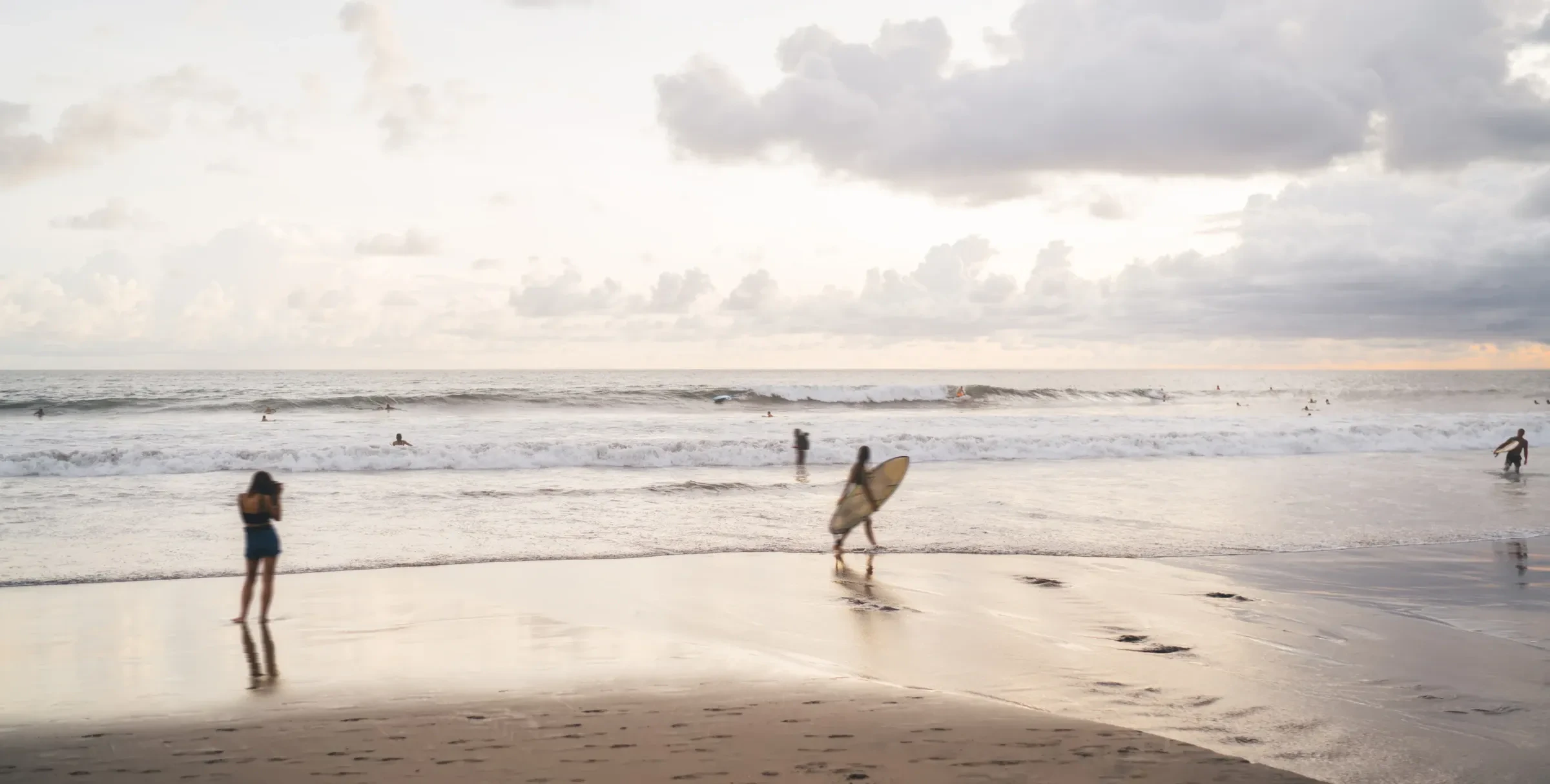 Surfers walking along a wide Bali beach at sunset with their boards