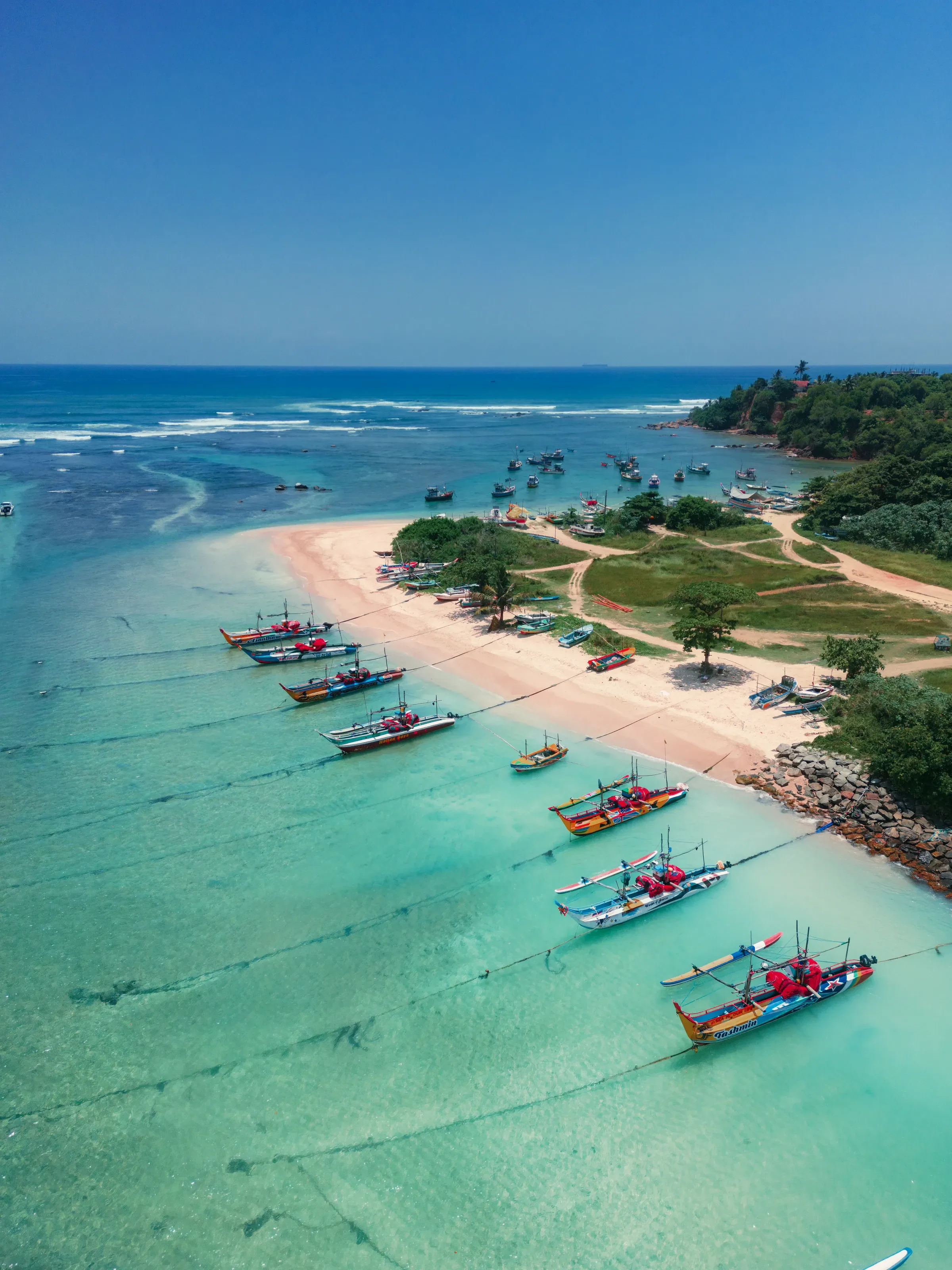 Weligama's long sandy beach from above, with outrigger boats lined up in the shallows