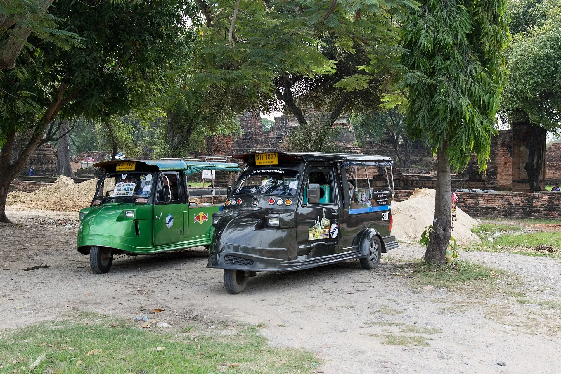Two tuk-tuks parked under trees near temple ruins in Ayutthaya