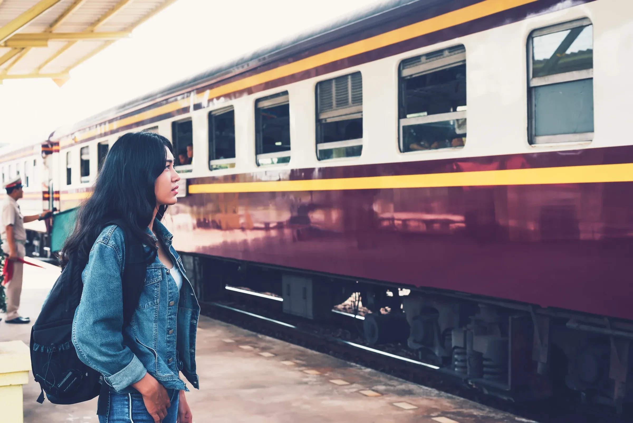 A backpacker waiting on a station platform beside a passenger train